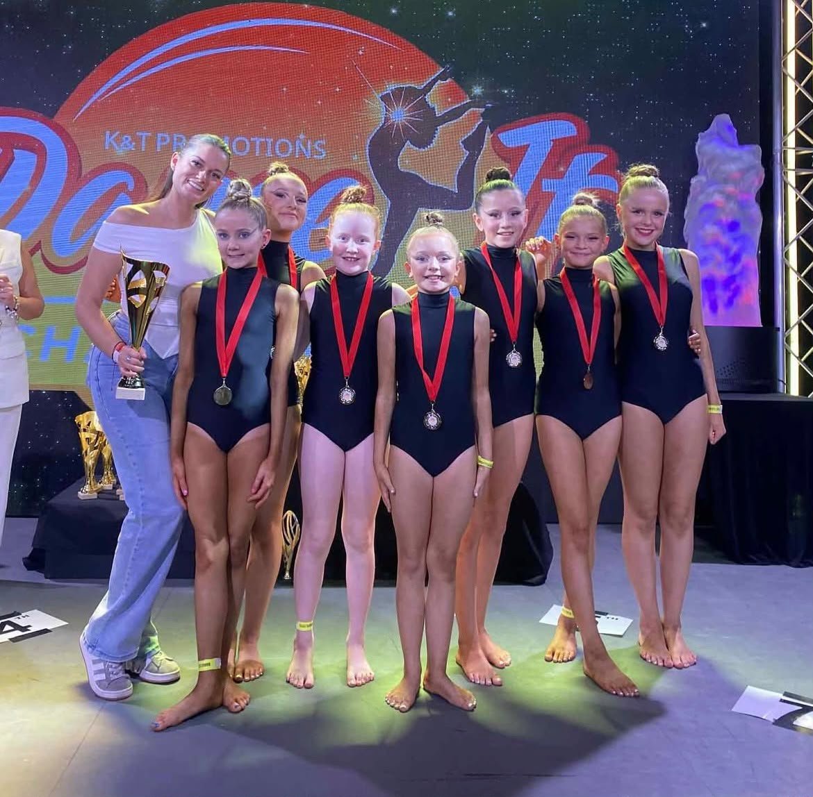 Youth dance team posing with medals and trophies onstage at a competition