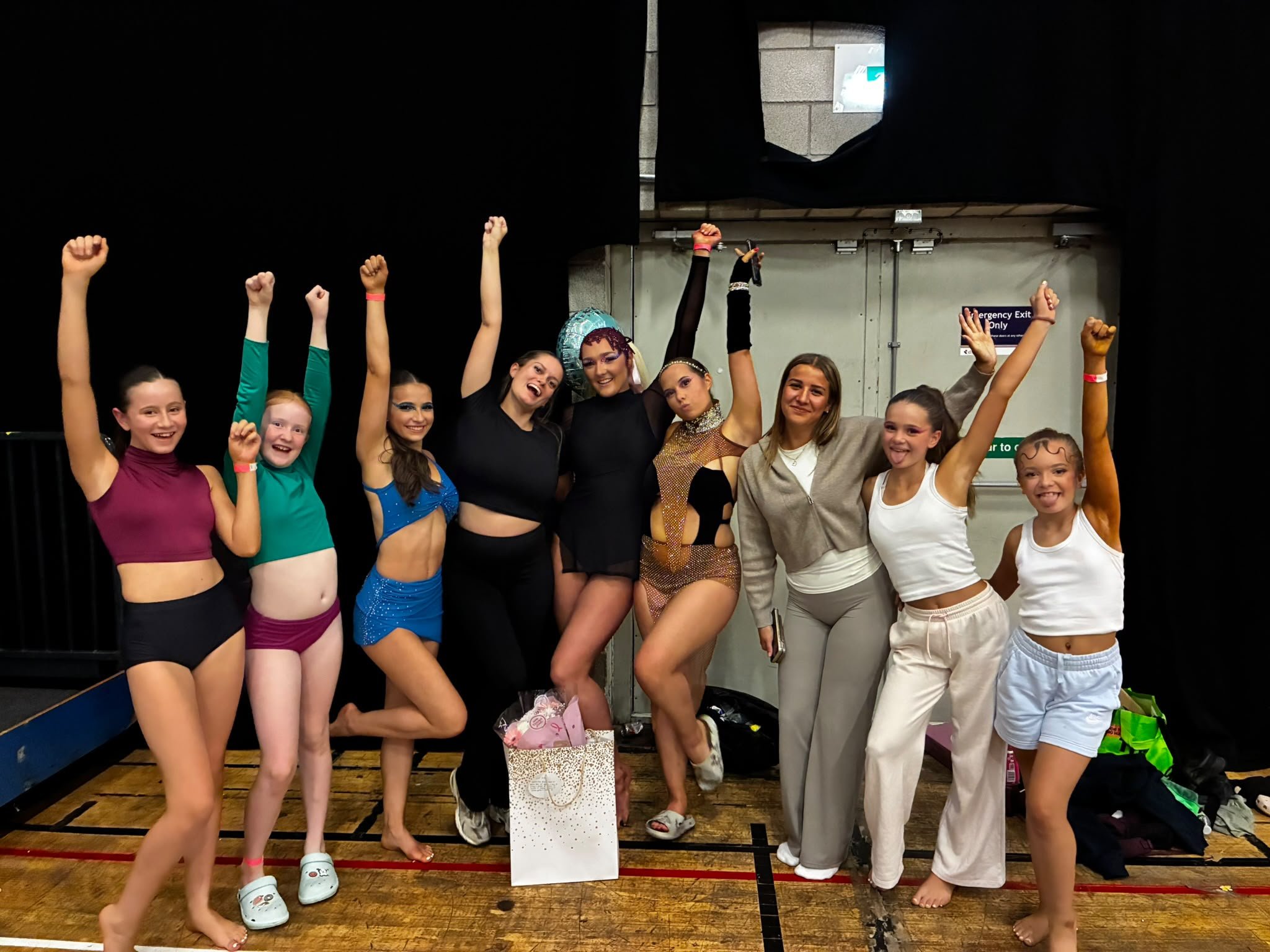 Group of dancers posing backstage with raised fists after a performance