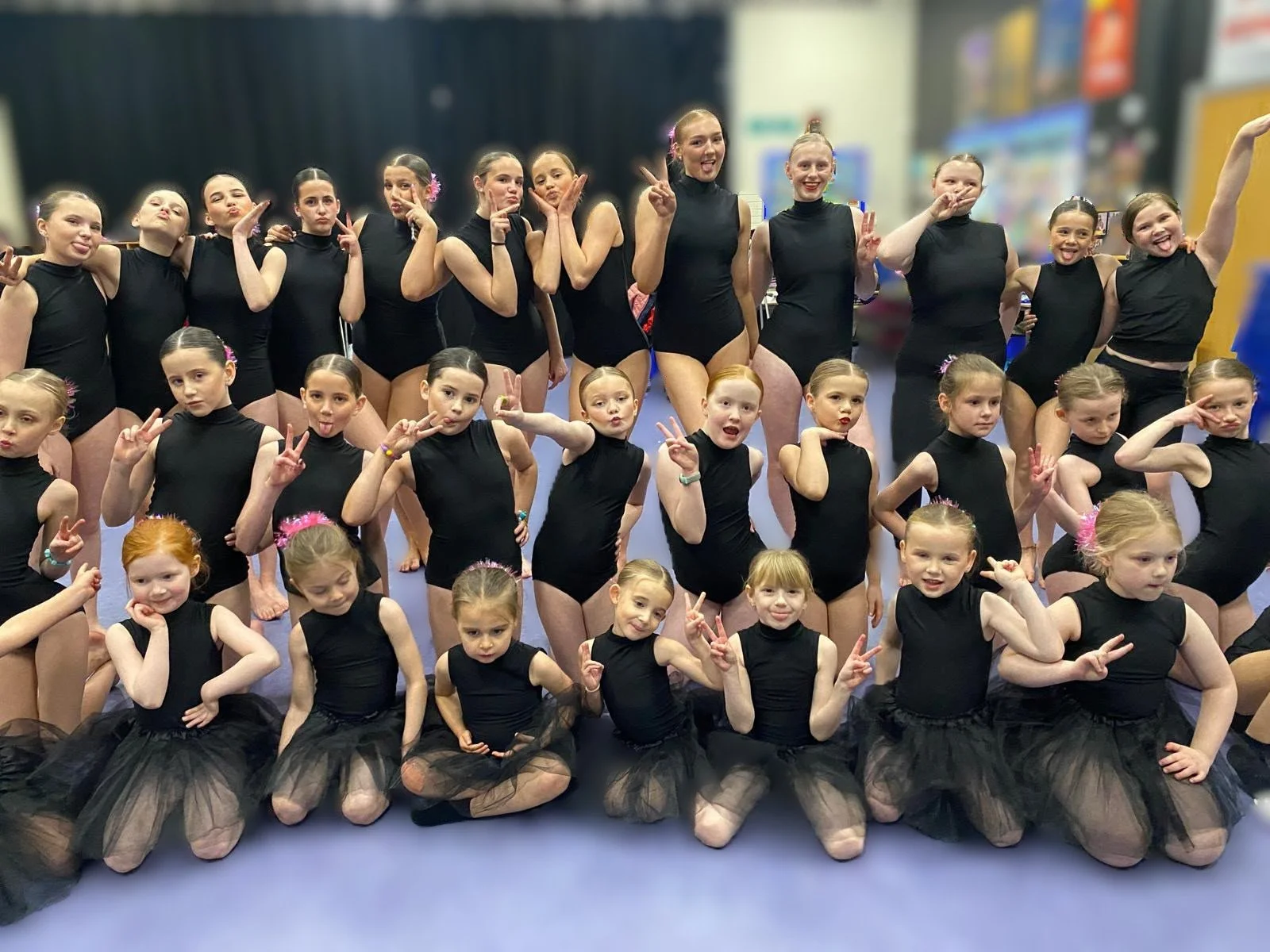Group of young dancers in black costumes posing together in a dance studio