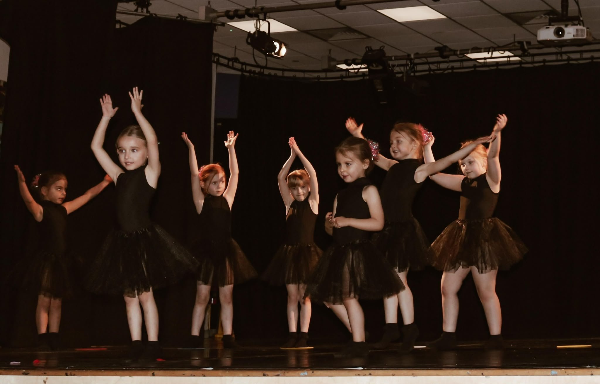 Young ballet dancers in black tutus performing on a theater stage under spotlights