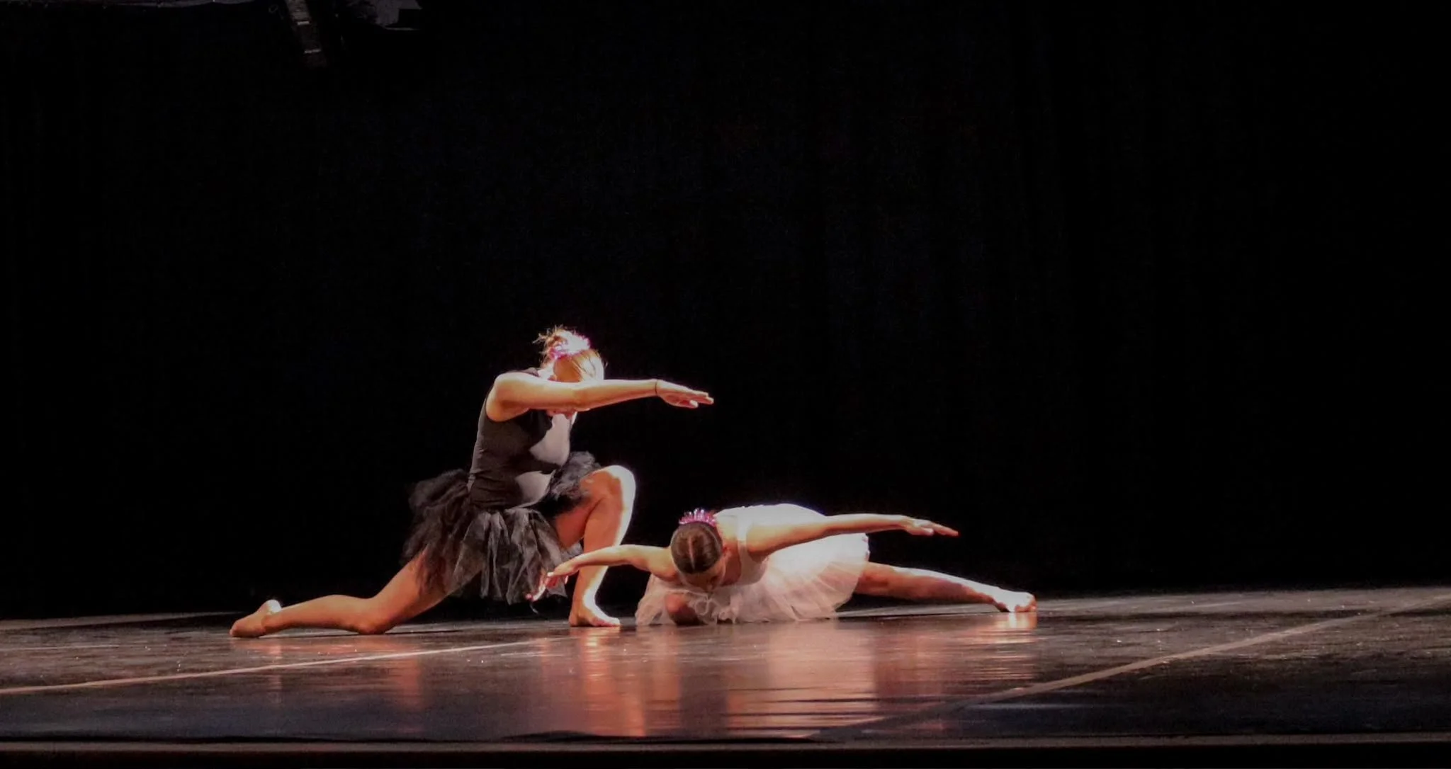 Two ballet dancers performing a dramatic floor pose on a dimly lit theater stage.