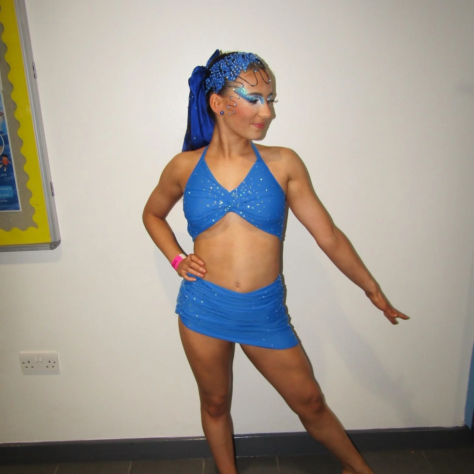 Woman posing in a sparkly blue dance costume with matching headpiece and stage makeup