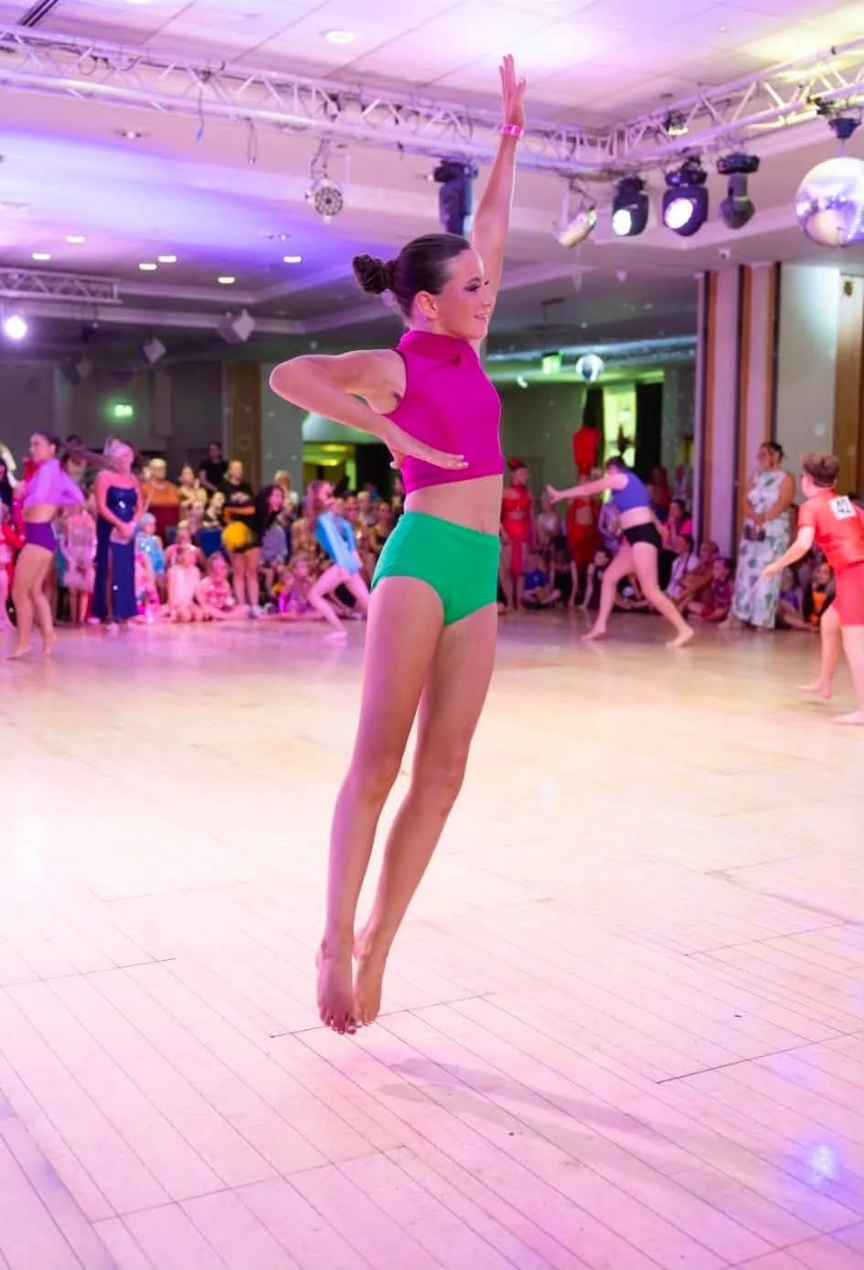 Ballet dancer in a pink top and green shorts leaping at a brightly lit dance performance