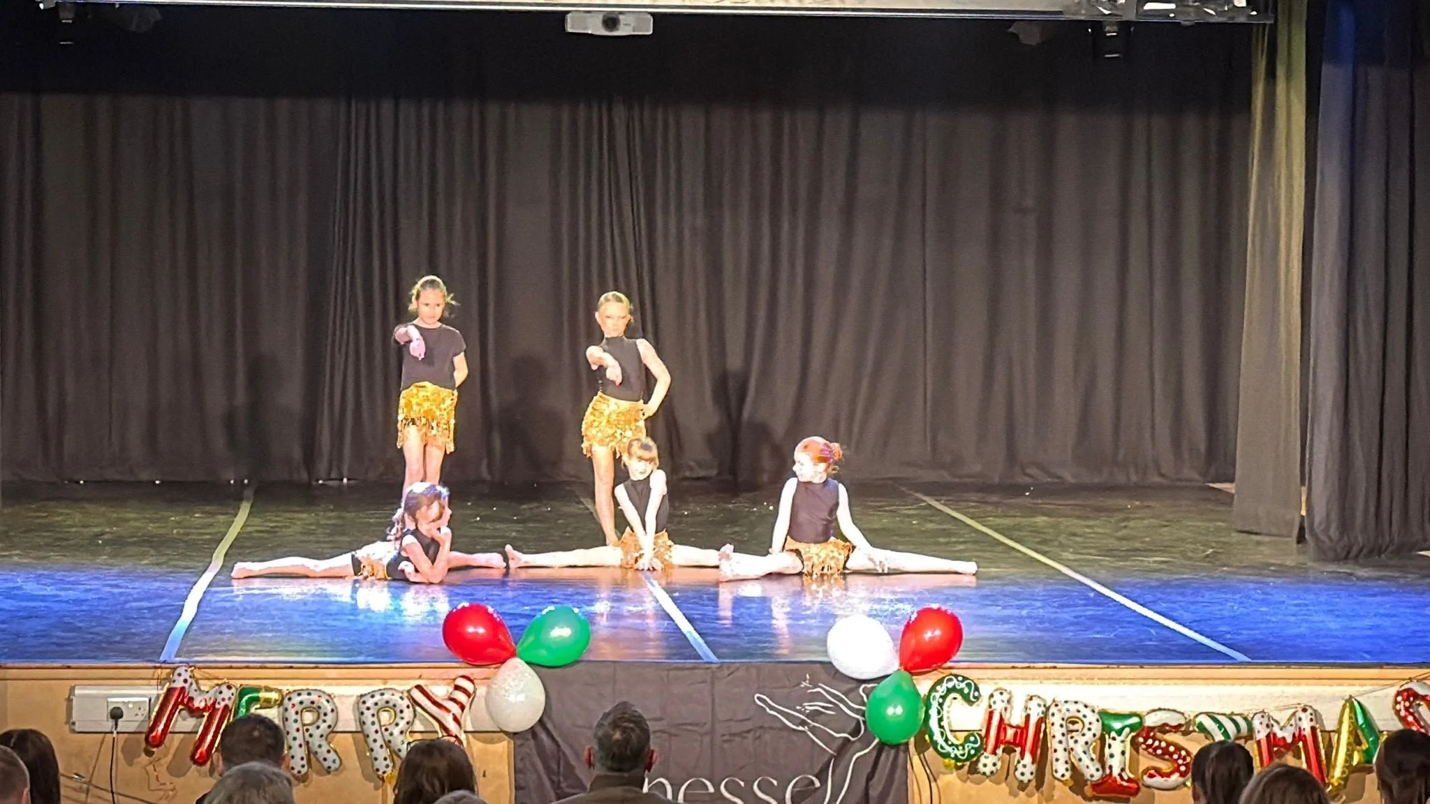 Children performing a dance routine onstage in gold costumes before a seated audience