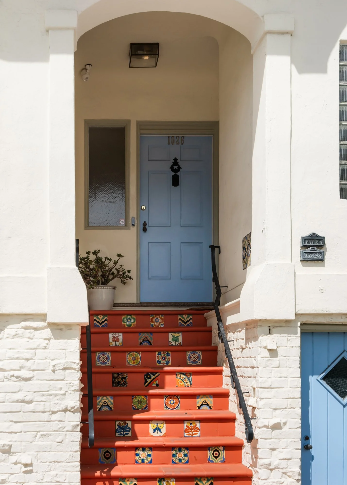 Front door with colorful tile stairs leading up to it, a potted plant on the porch, and house number 1026.