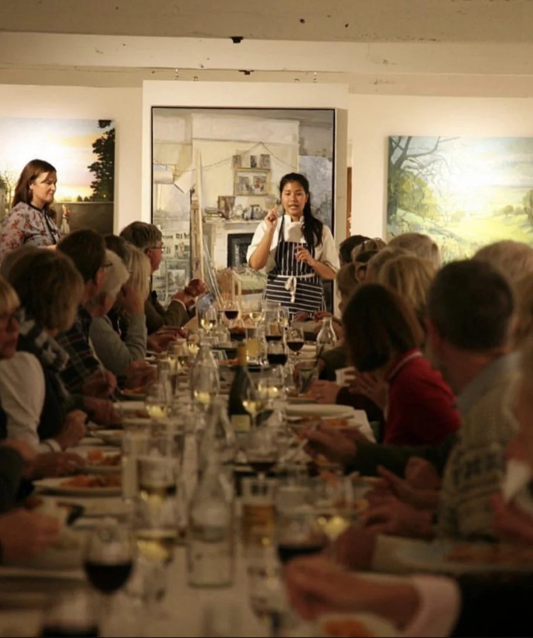 A woman giving a presentation or speech in front of a dining group in a restaurant or banquet hall.