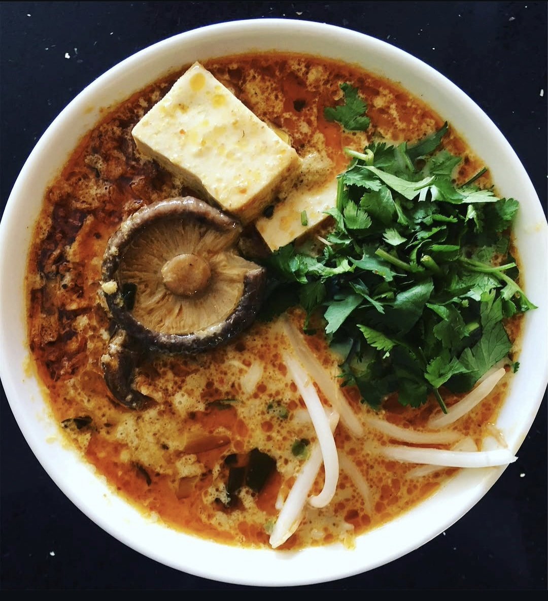 A bowl of spicy Vietnamese noodle soup with tofu, mushrooms, bean sprouts, and fresh cilantro.