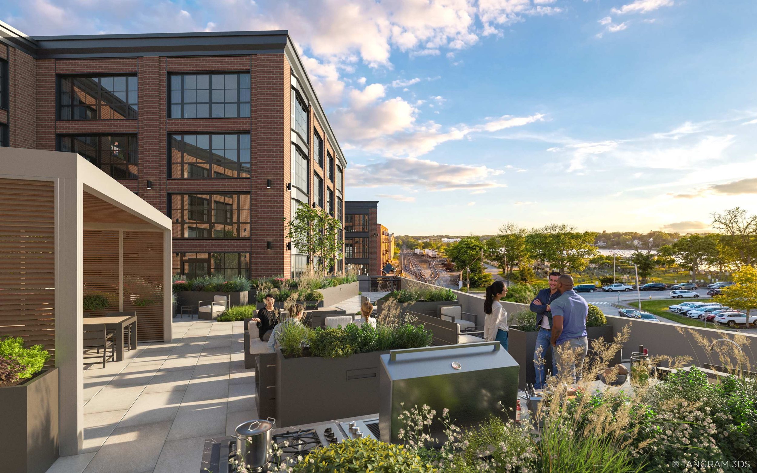 People gather on a rooftop terrace at sunset, with modern brick apartment buildings and a parking lot in the background.