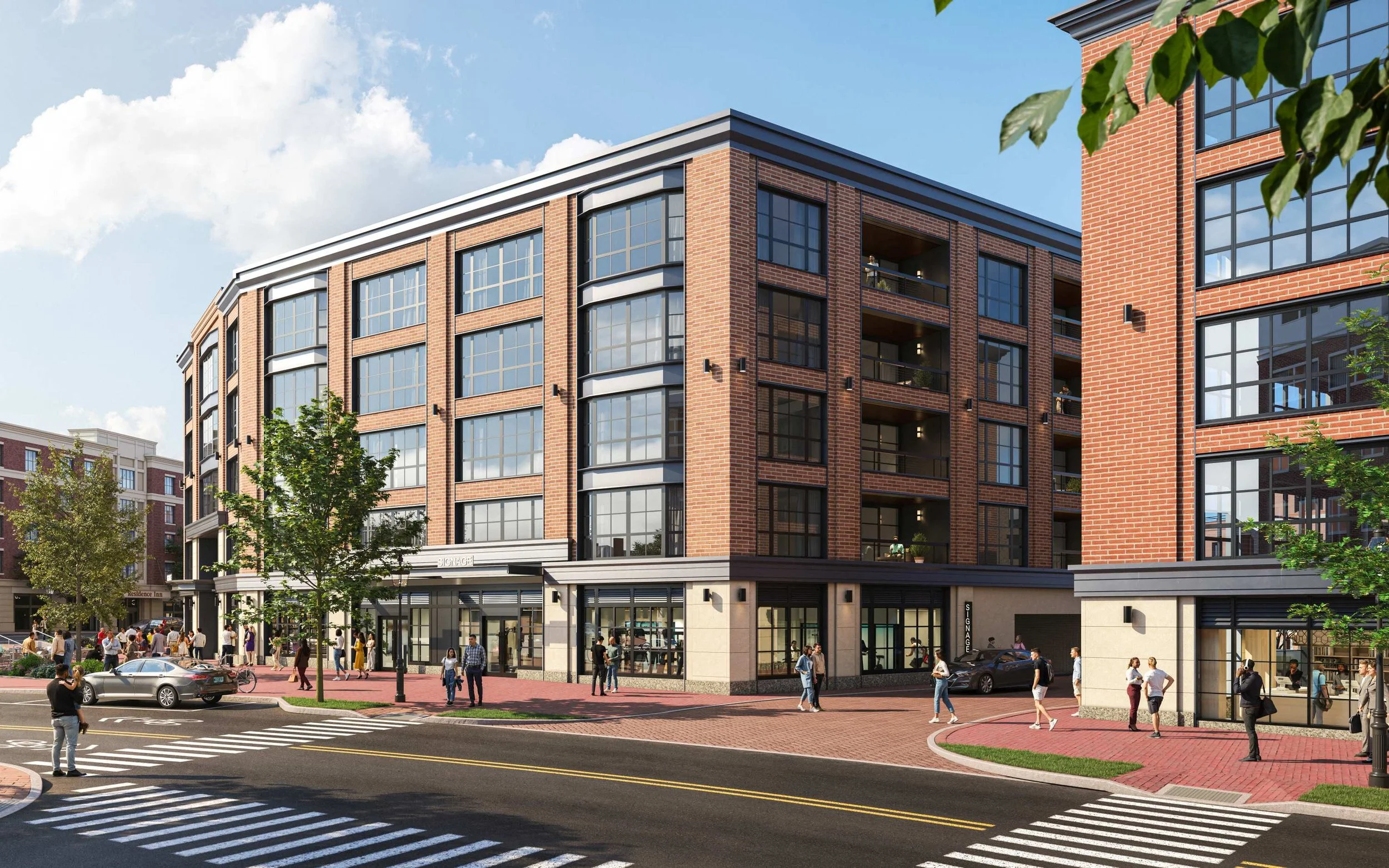 Modern multi-story brick building with large windows and retail spaces on the ground floor. People walking on the sidewalk, cars parked, and trees along the street under a partly cloudy sky.