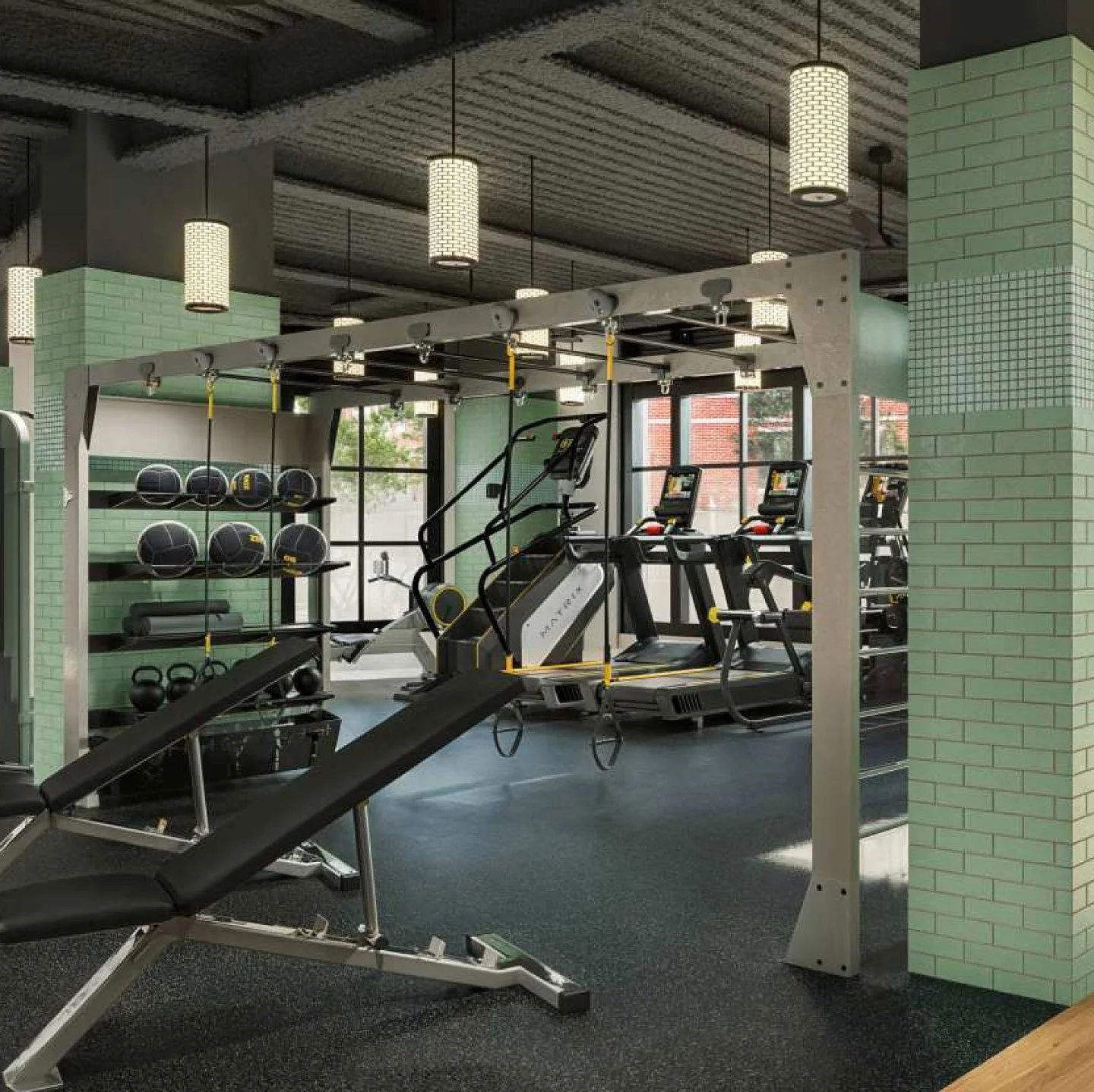 Inside a modern gym featuring treadmill, exercise bikes, kettlebells, medicine balls, and a workout bench. The gym has green brick walls, hanging ceiling lights, and large windows.