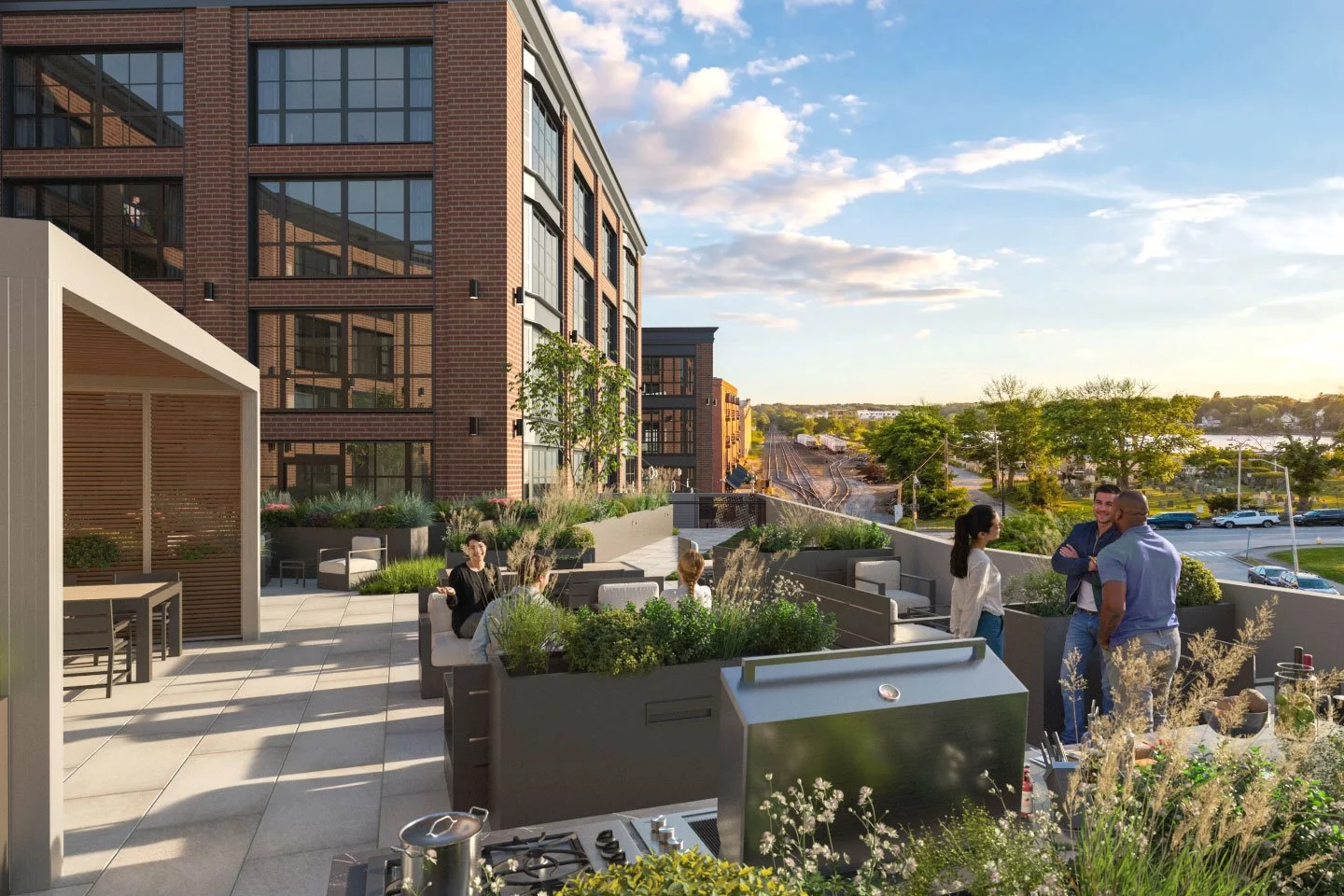 People socializing on an outdoor rooftop patio in the evening with modern furniture, greenery, and a cityscape in the background.