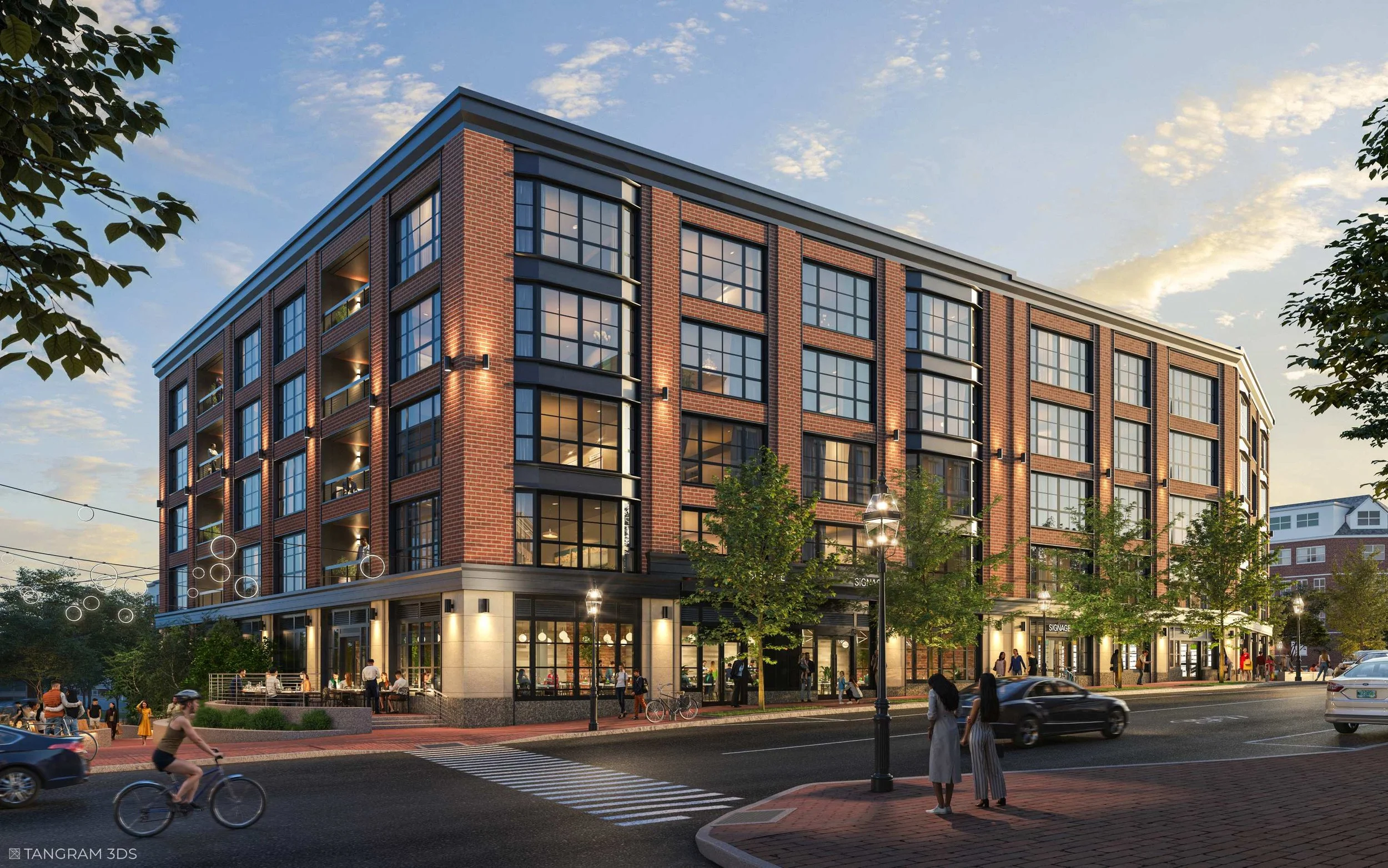 A modern brick building with large windows on a city street at dusk. People are walking and riding bicycles nearby, and streetlights illuminate the area.