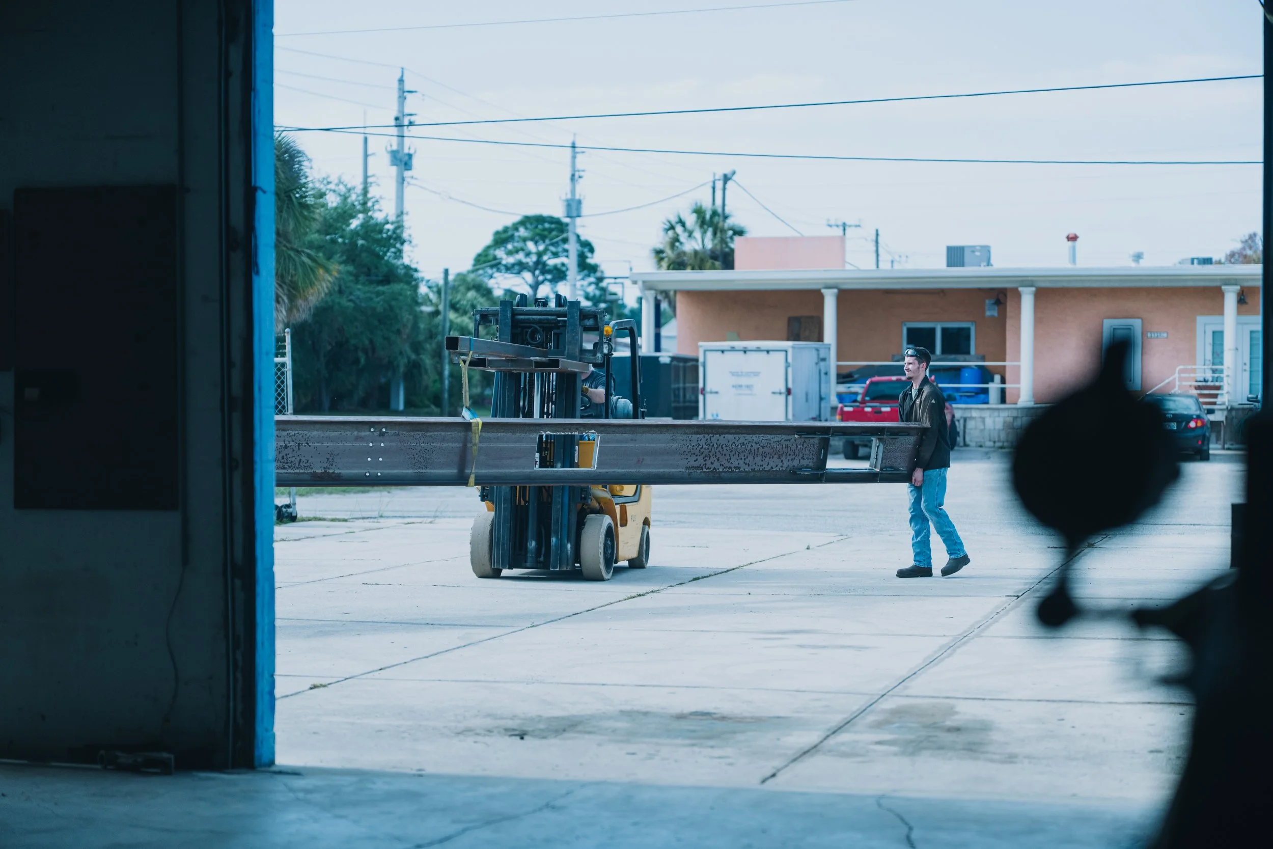 A man walking outside near a forklift in a residential area, seen through a doorway or window.