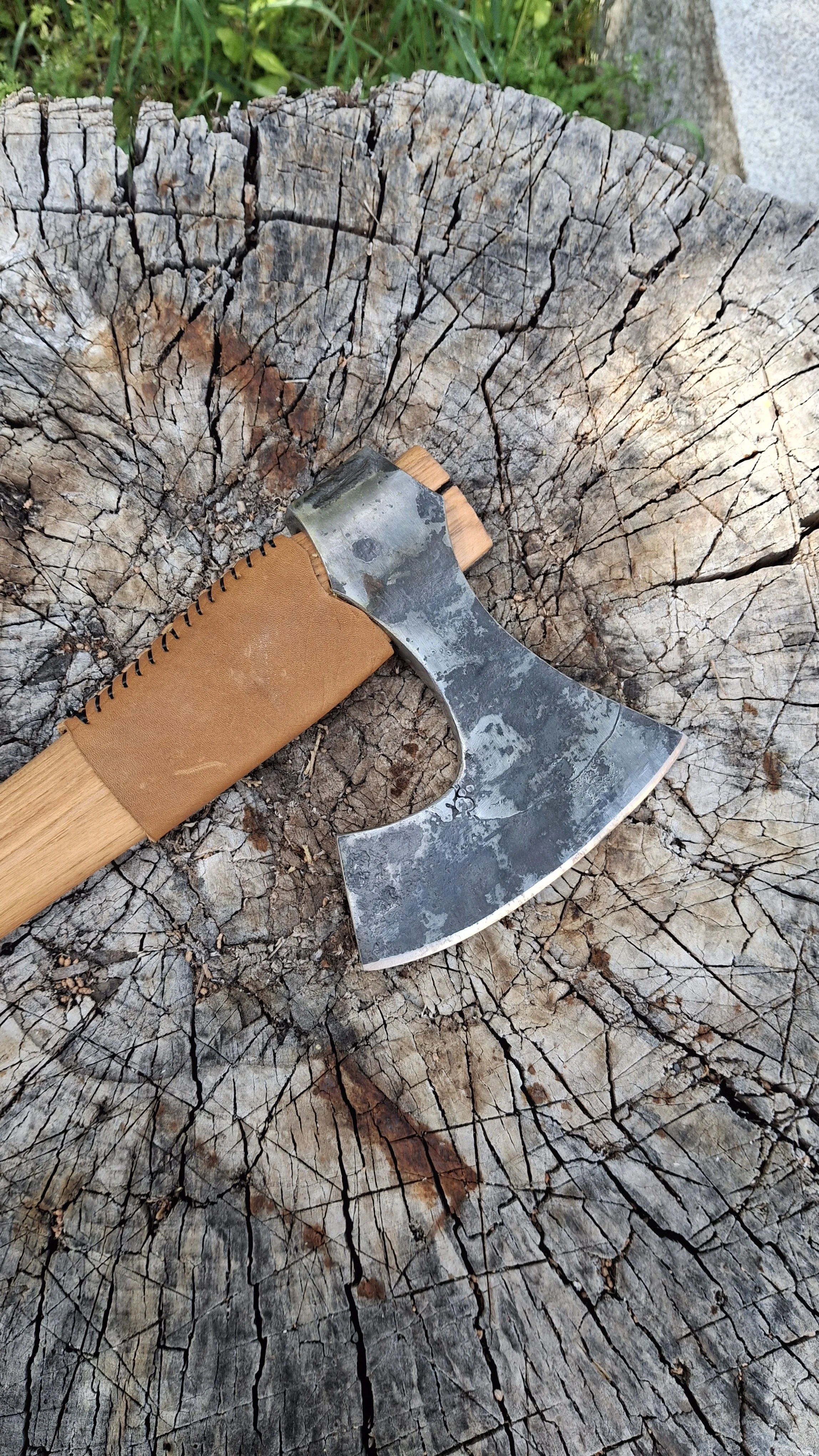 A viking style bearded axe with a metal head and wooden handle resting on a cracked, weathered tree stump.