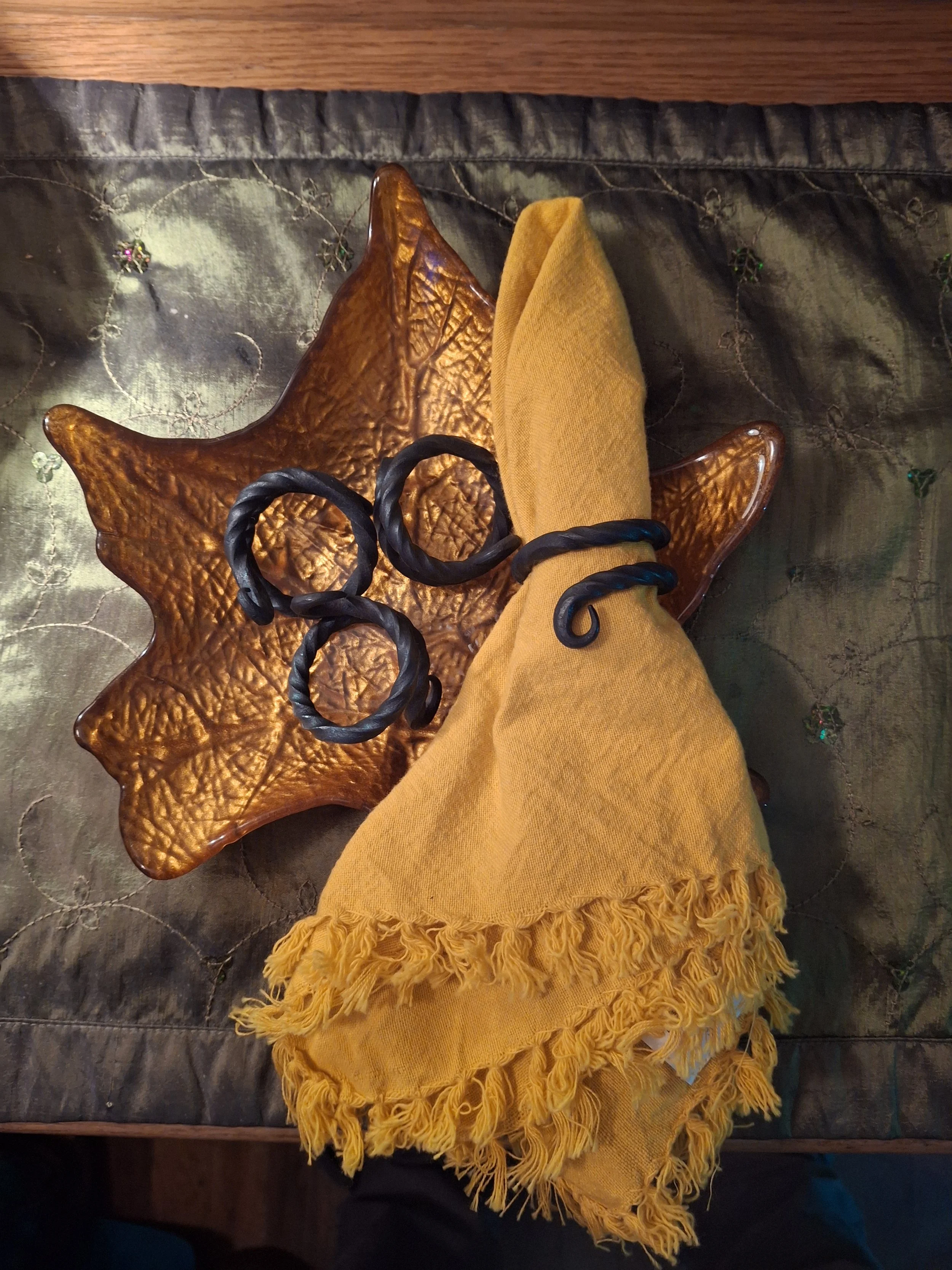 A yellow fringed scarf draped over a star-shaped wooden tray, with a yellow cloth and black twisted jewelry on top, placed on a dark quilted fabric.