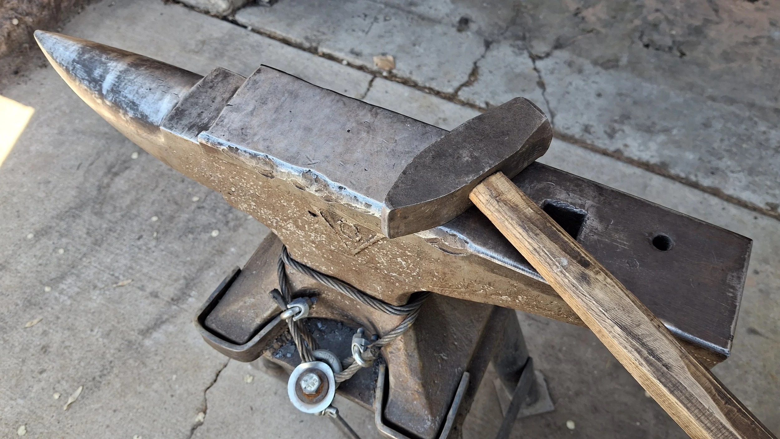 An anvil with a hammer resting on it. The anvil appears well-used with scratches and wear.