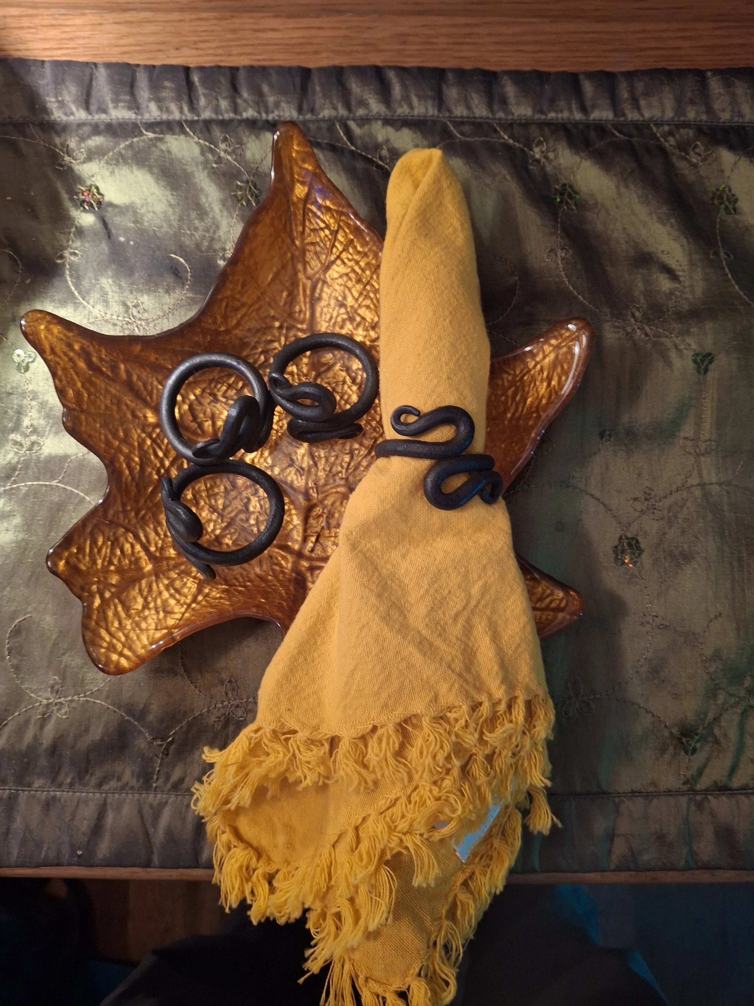 View from above of a brown leather star-shaped bowl holding a yellow cloth napkin and black decorative objects on a black quilted surface with embroidered flower designs.