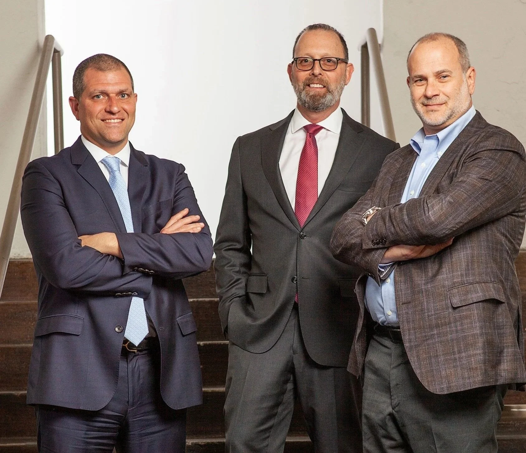 Three men in business suits standing on stairs with arms crossed.