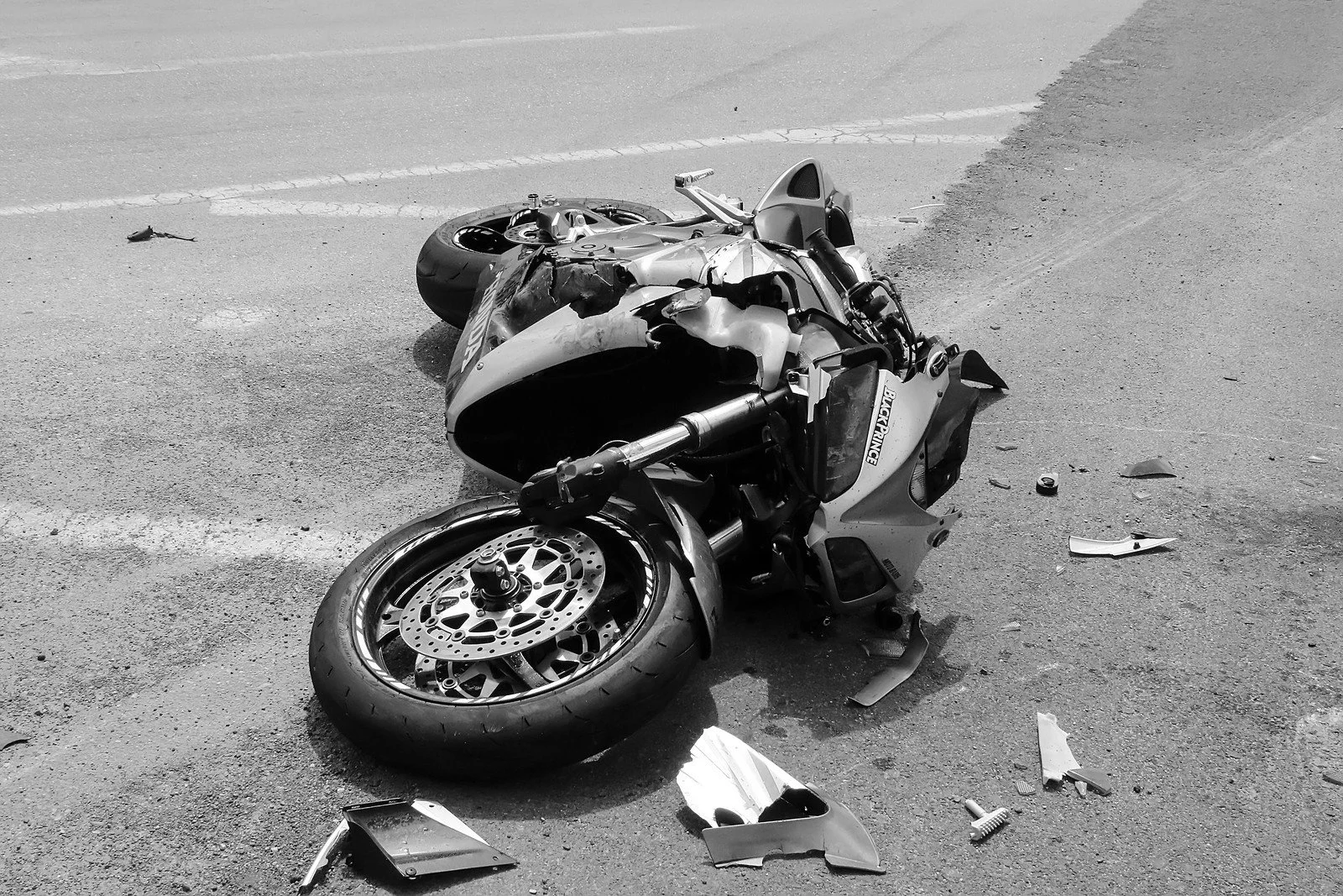A severely damaged motorcycle lying on its side on the road with scattered debris around it, indicating a crash.