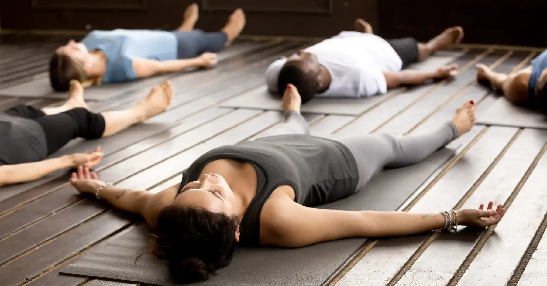 People lying on yoga mats in a yoga class, practicing relaxation, meditation, and receiving a sound bath.