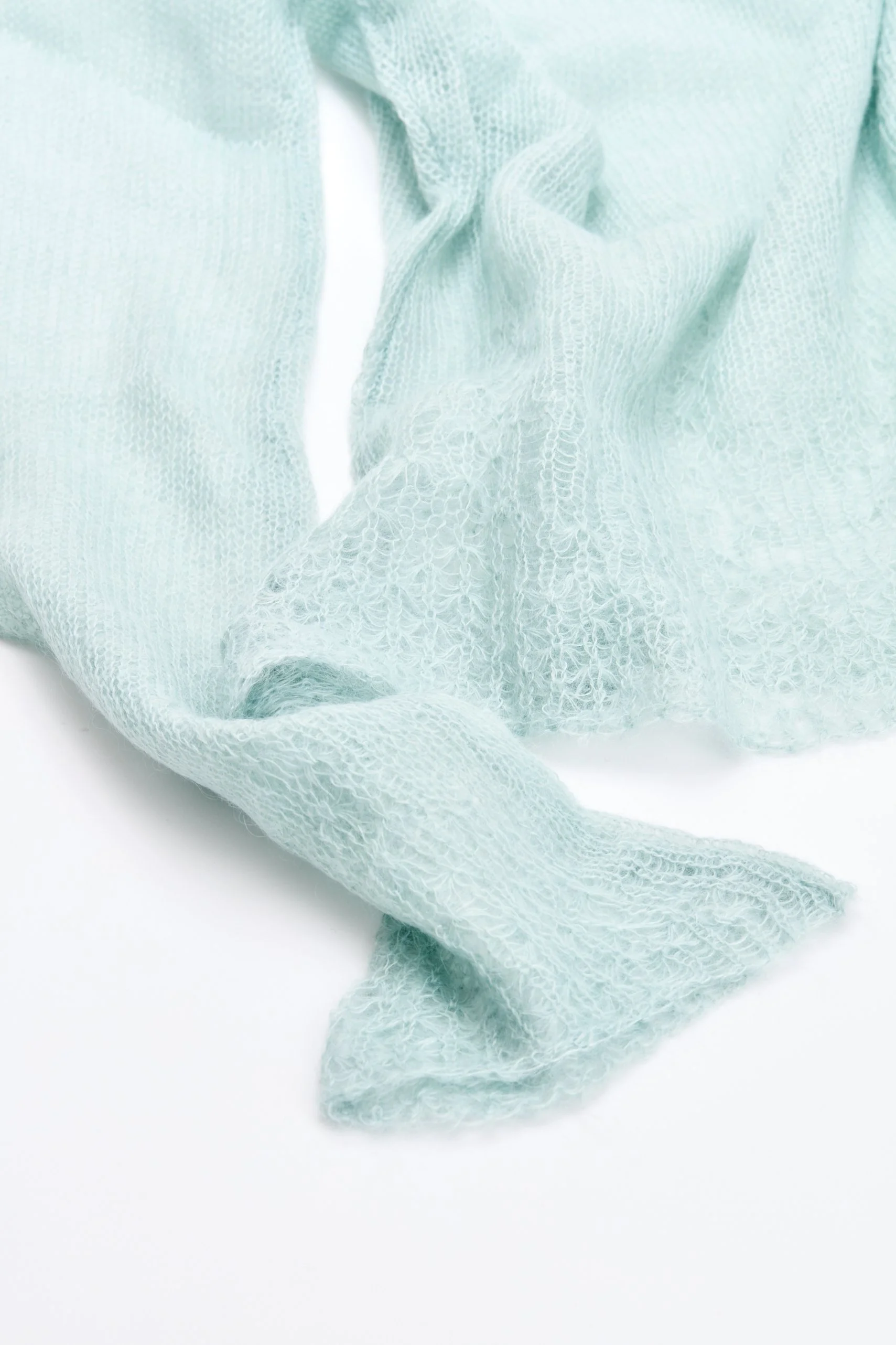 Detalhe de peça em trico de mohair rendado azul claro e delicado, com textura leve e transparente, formando dobras e curvas suaves.