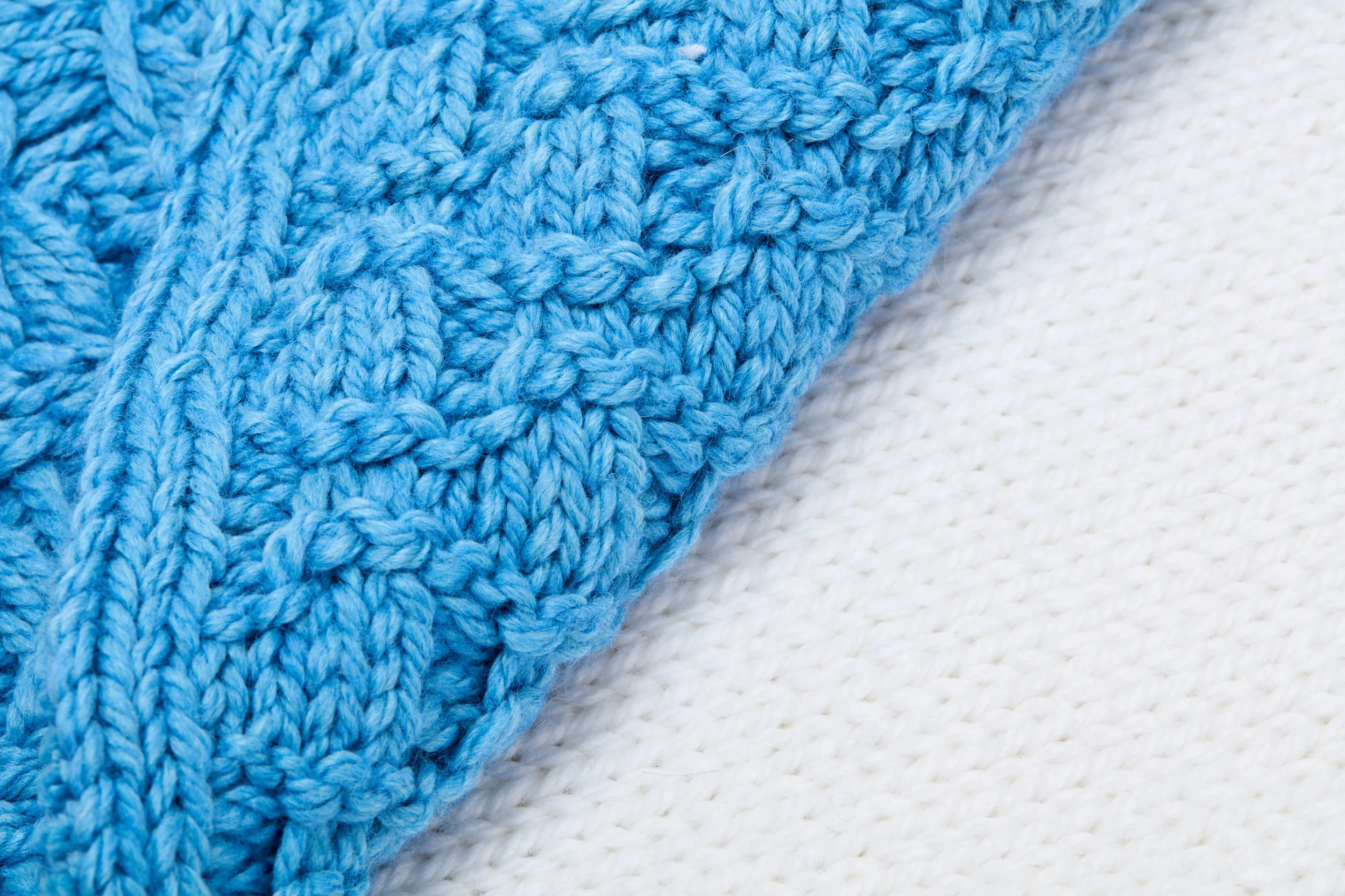 Close-up de duas peças de tricô, uma azul clara e outra branca, mostrando detalhes das linhas e texturas do tecido.