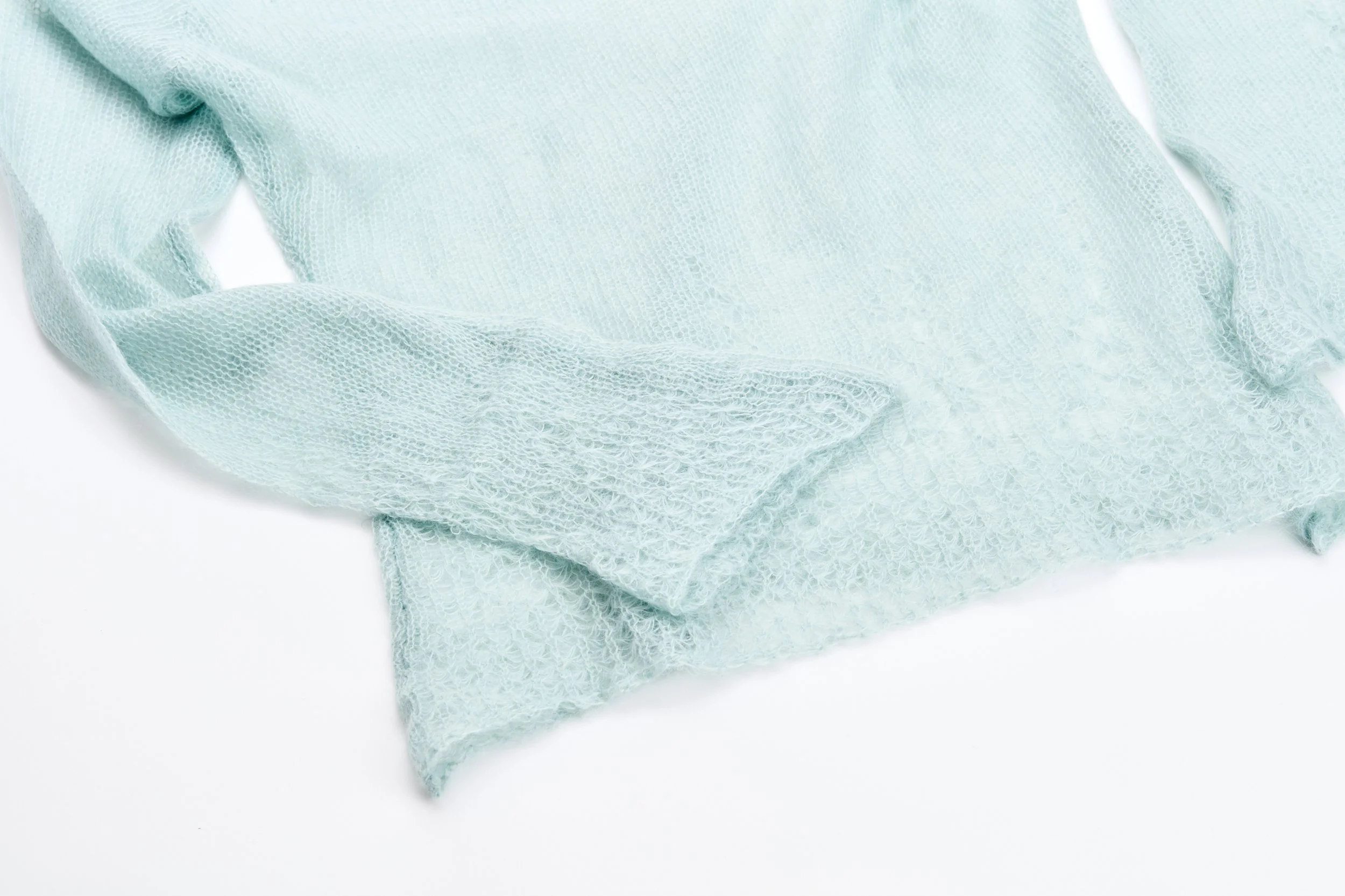 Tecidos de cor azul claro com textura de malha suave, dispostos em camadas sobre fundo branco.
