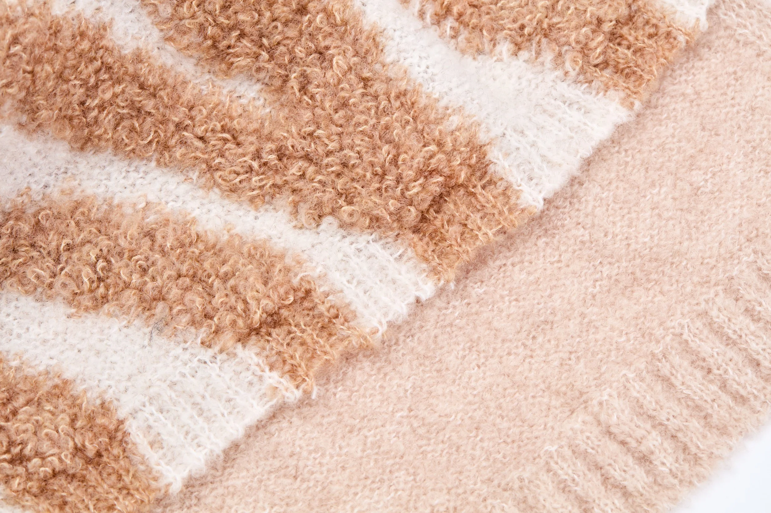 Imagem de uma textura de tecido aconchegante, com partes de pelúcia e tricot em tons de bege, branco e caramelo.