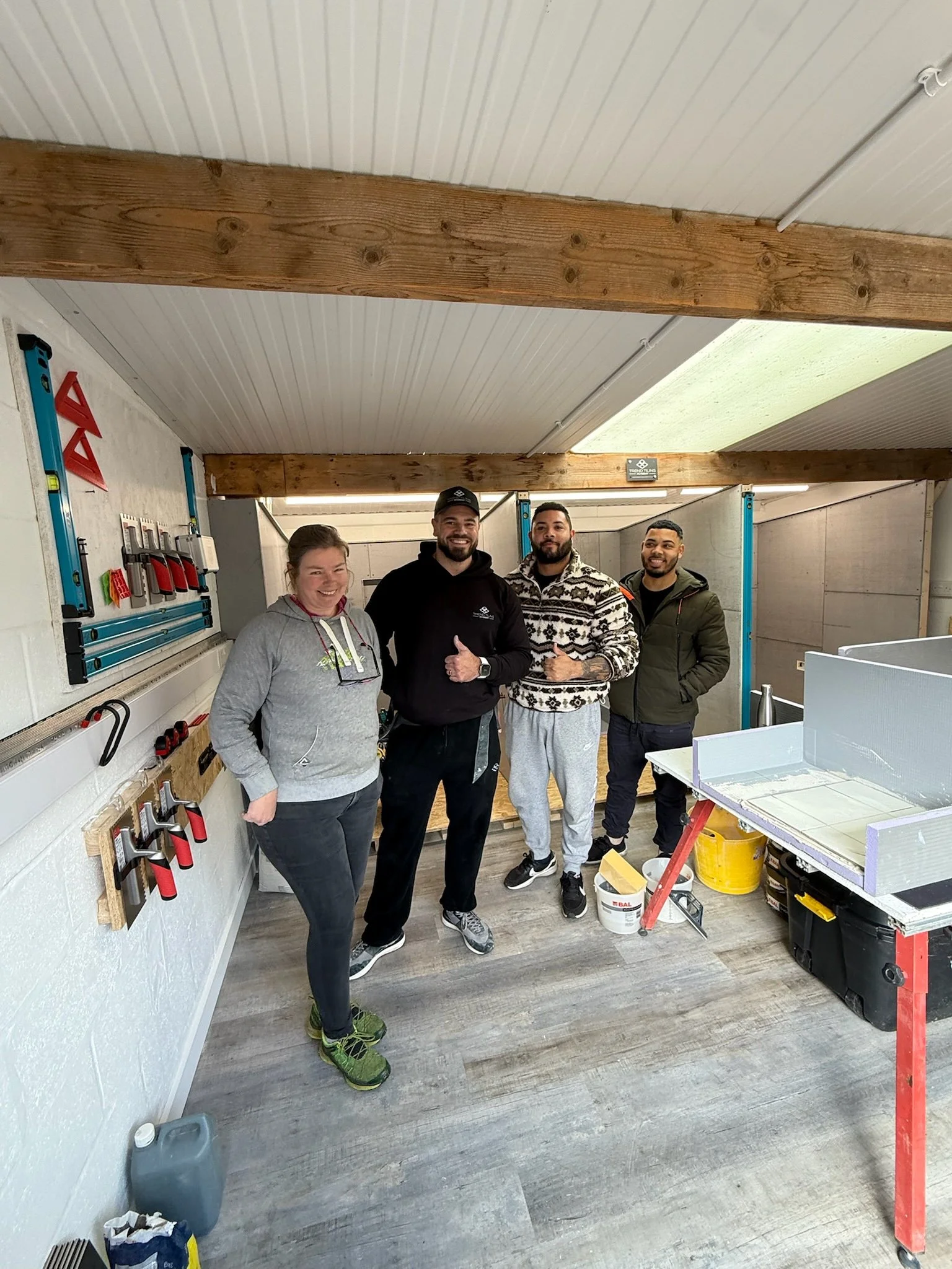 Four people standing in a room with tools and construction materials, smiling and posing for a photo.