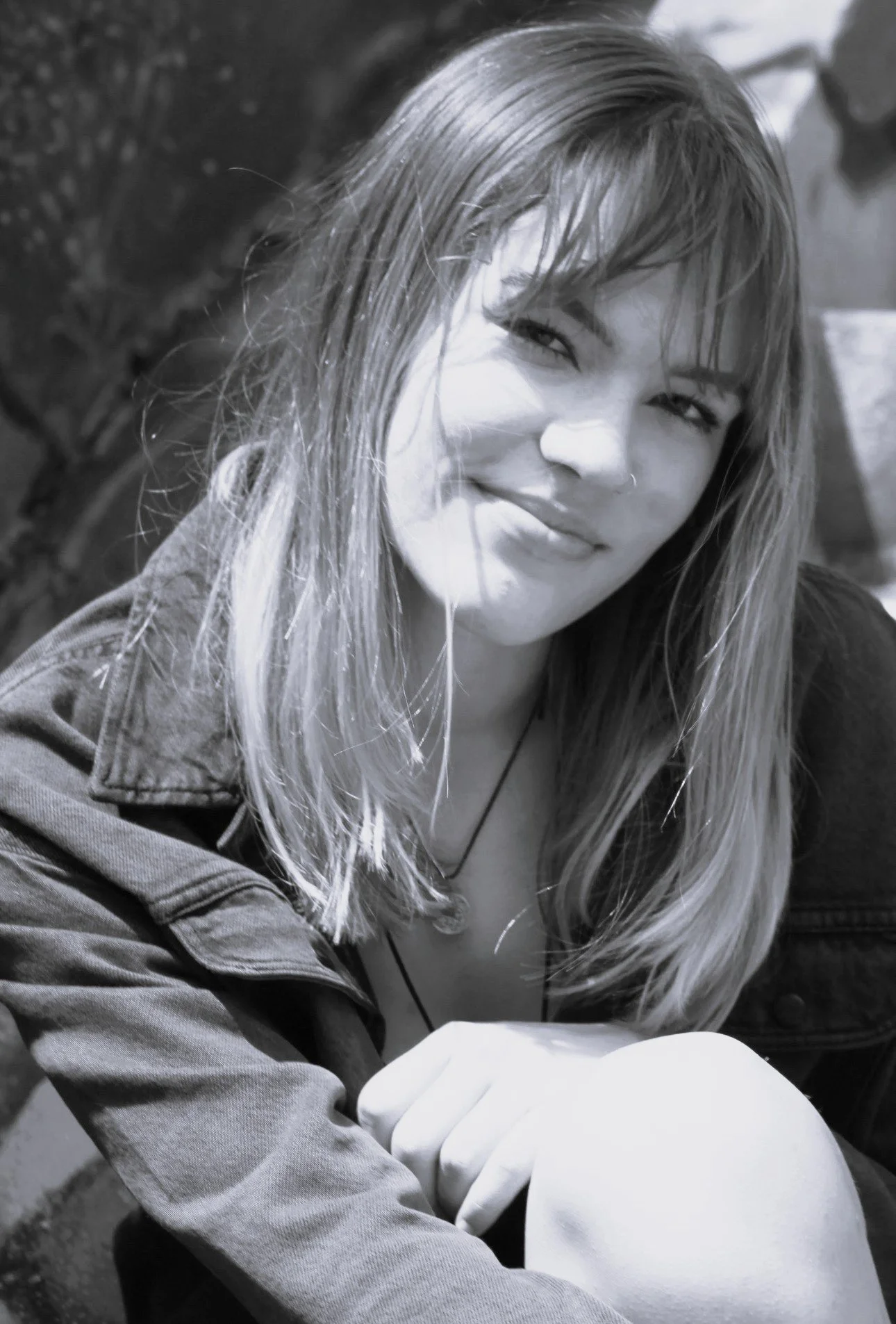 A young woman with long straight hair smiling at the camera, wearing a sleeveless top, in black and white.