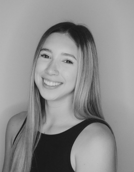 A young woman with long straight hair smiling at the camera, wearing a sleeveless top, in black and white.