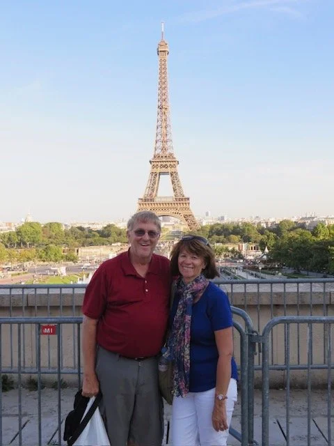 A couple standing in front of a metal railing with the Eiffel Tower in the background in Paris, France.