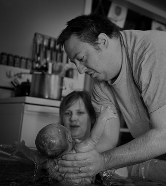 A man and a woman lifting a newborn baby out of a birthing tub in their home.