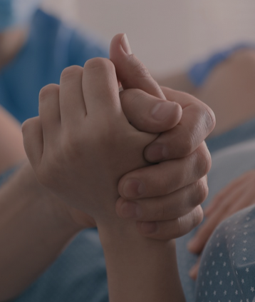 Two people holding hands, one with a hospital bracelet on the wrist.