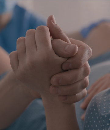 Two people holding hands, one with a hospital bracelet on the wrist.
