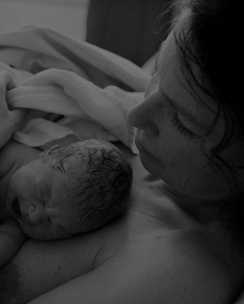 A woman holding a newborn baby close to her face, both lying in a hospital bed, in a black and white photo.