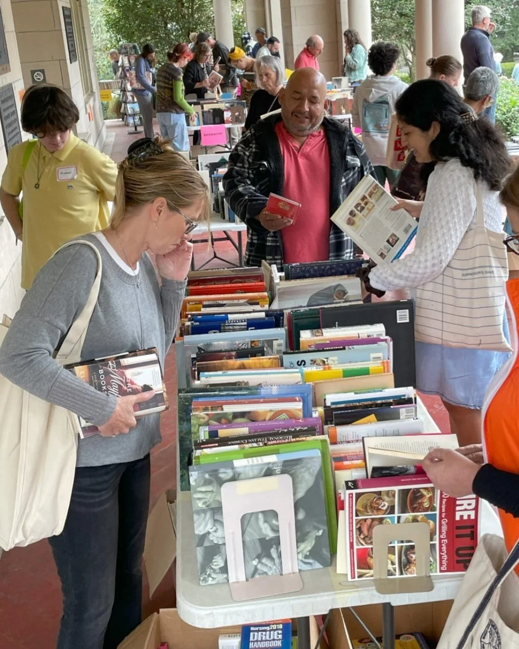 People shopping for books at an outdoor book fair, browsing shelves and tables filled with books.
