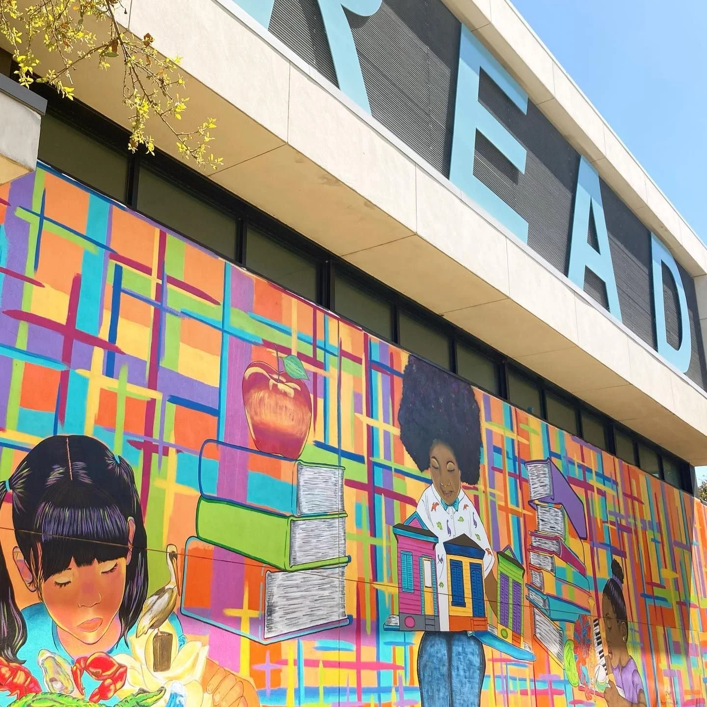 Colorful mural on the library building featuring children reading books, a stack of books, and a schoolhouse, with large blue letters spelling 'LEAD' above.