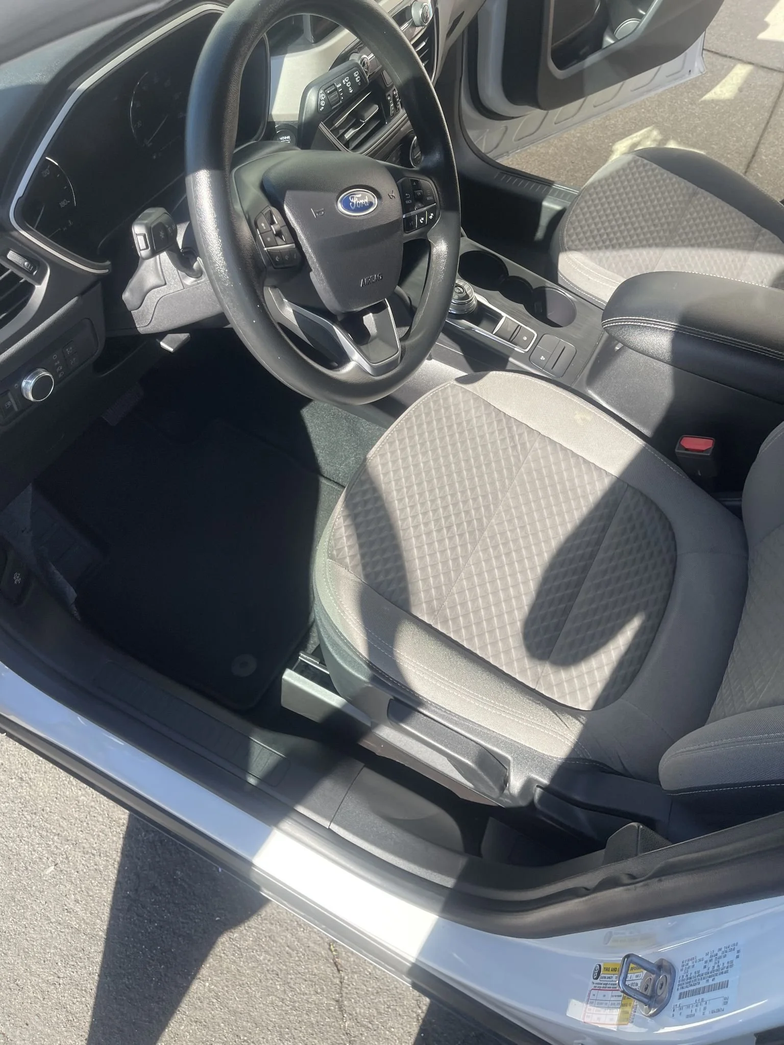 The interior of a Ford vehicle showing the steering wheel, dashboard, center console with gear shifter, and front passenger seat.