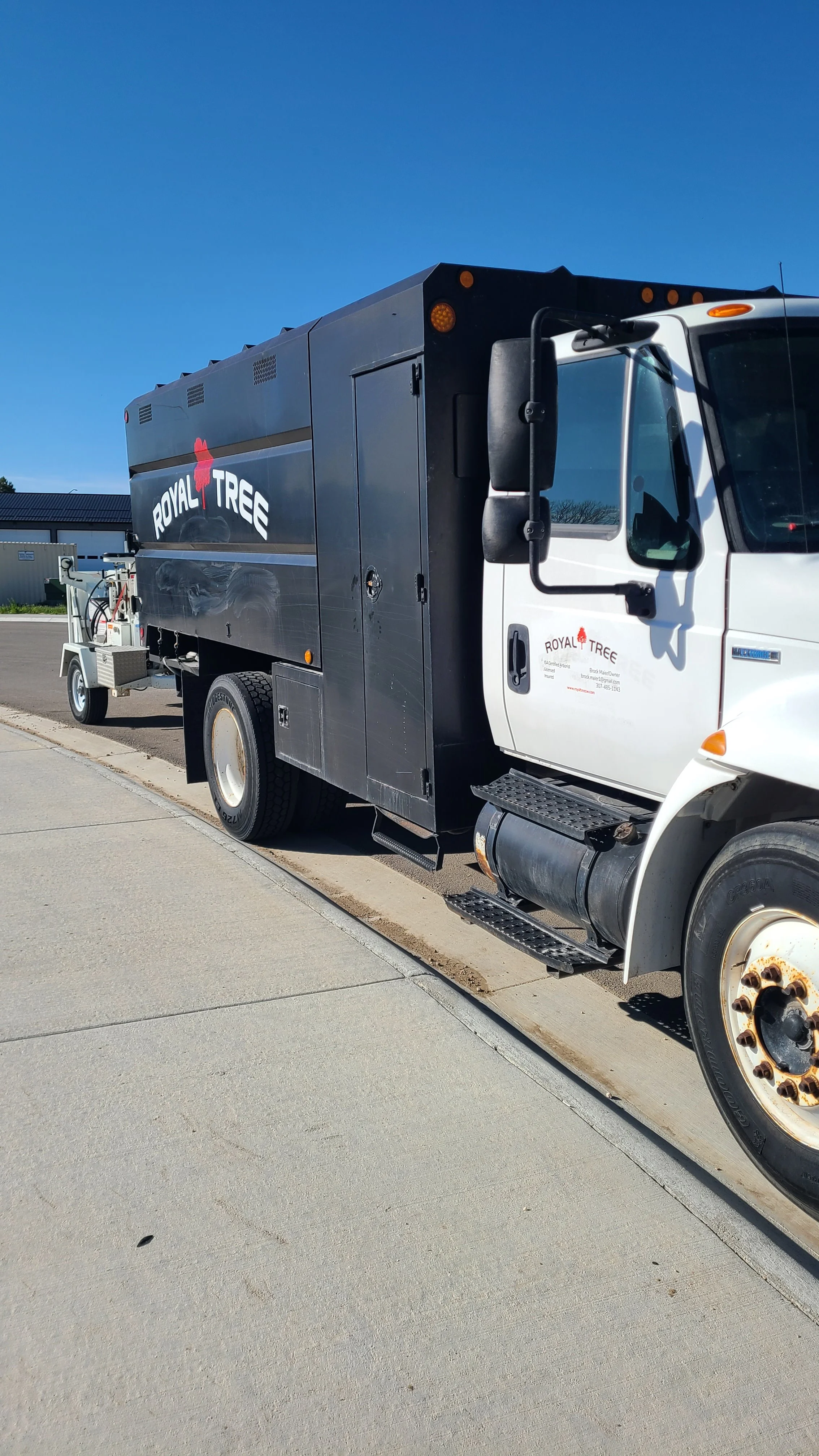 A black and white Royal Tree service truck parked on the side of a street under a clear blue sky.