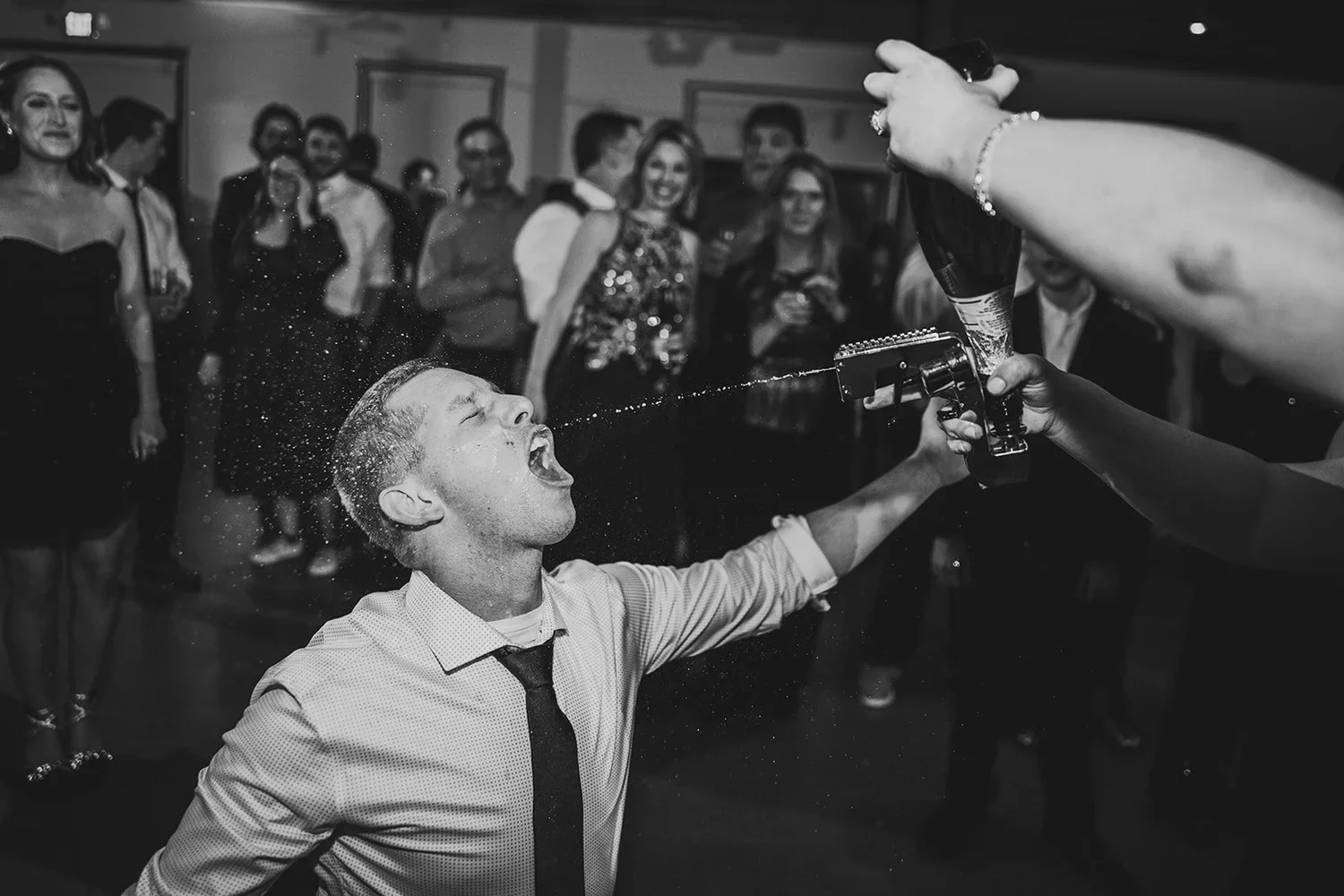Black and white wedding reception photo of guest taking a shot from a toy gun during the celebration.