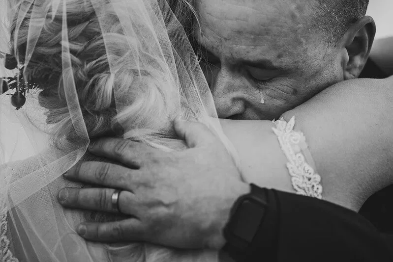 Black and white close-up wedding photo of a bride and her father embracing and sharing an emotional moment.