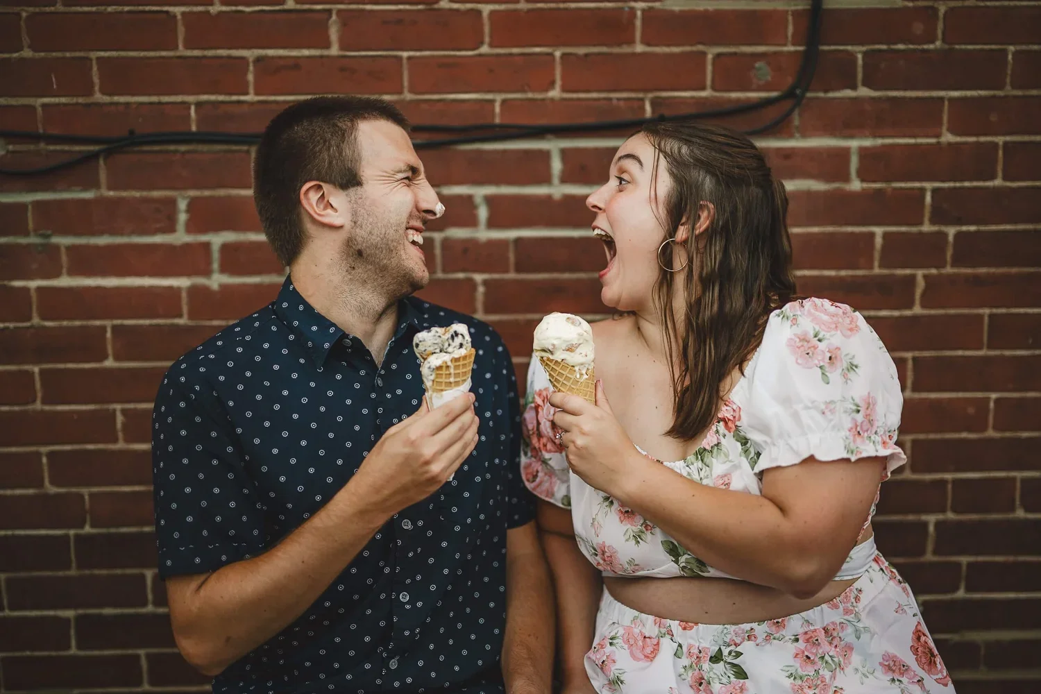 Couple smiling and looking at each other while eating ice cream cones during their engagement photoshoot.
