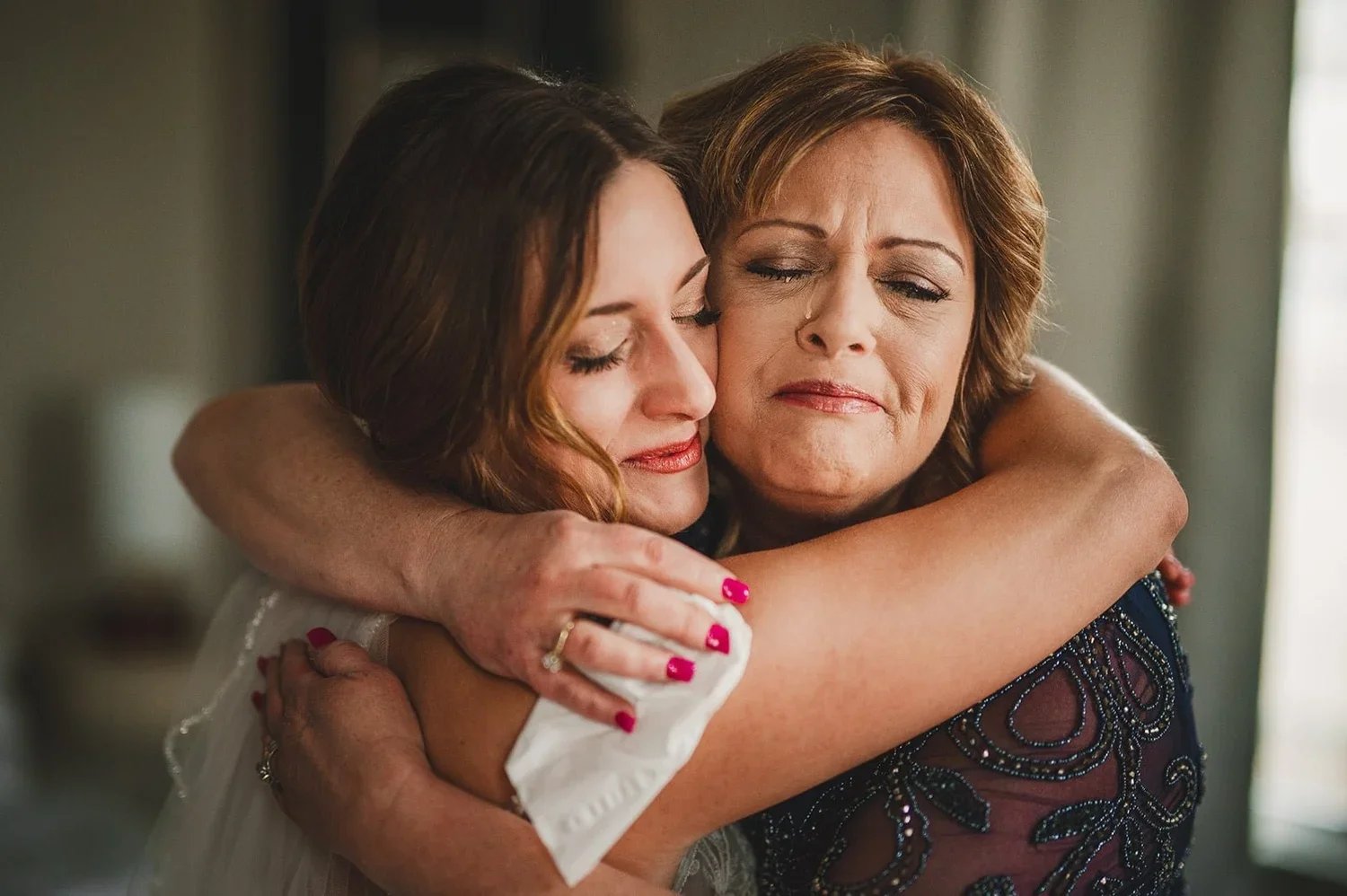 Emotional wedding portrait of a bride and her mother sharing a joyful embrace and smile.
