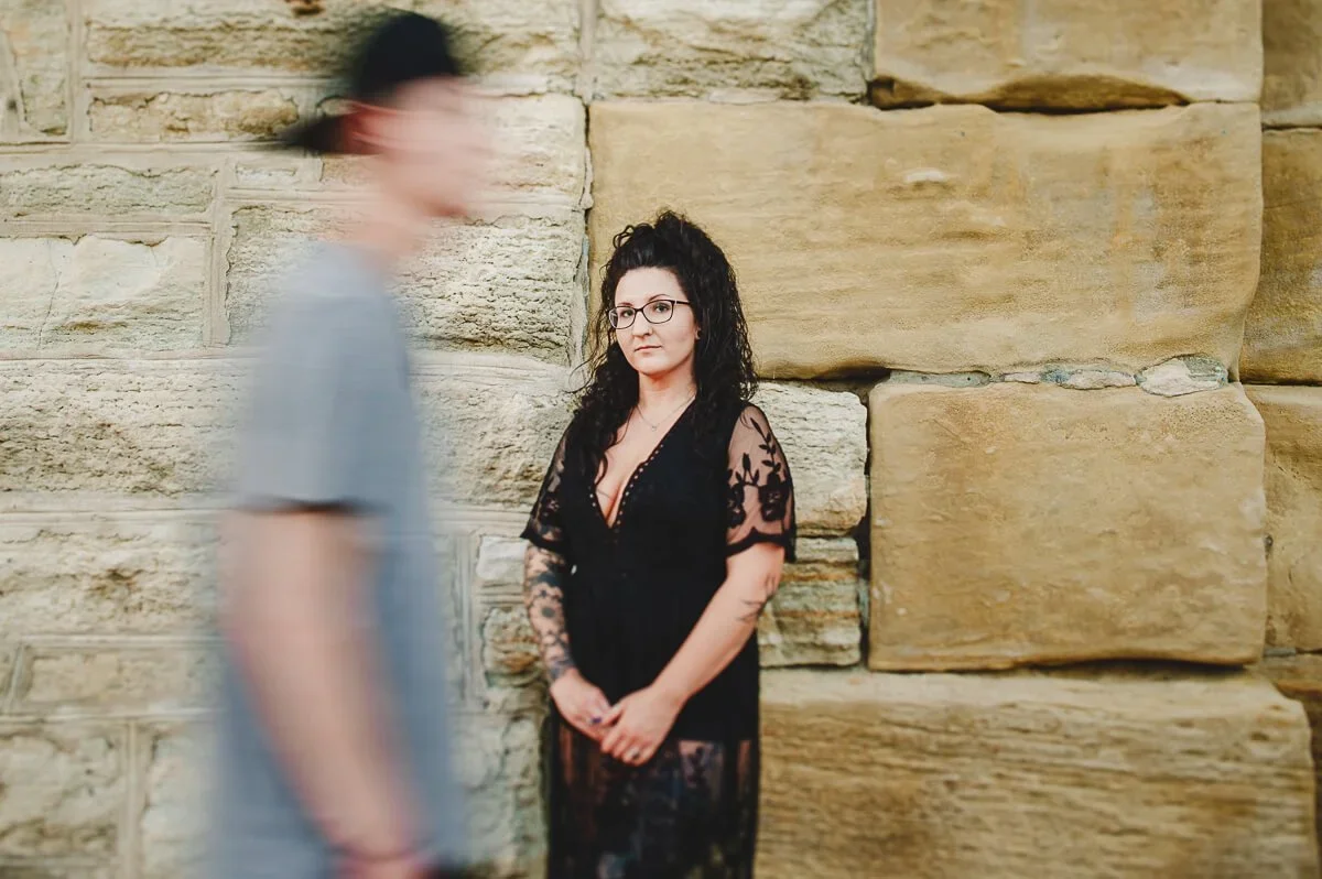 Woman wearing black standing in the center of the frame while a man walks by on the left with blurred motion.