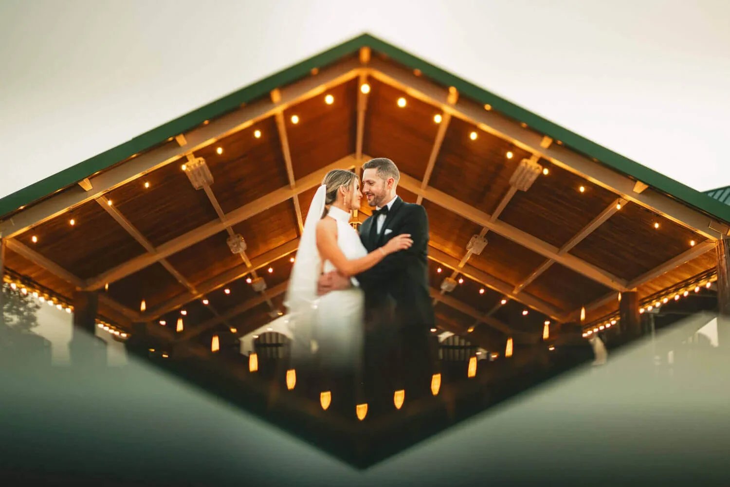 Wedding portrait of a bride and groom inside their venue with a dark wood background creating a reflective pattern.