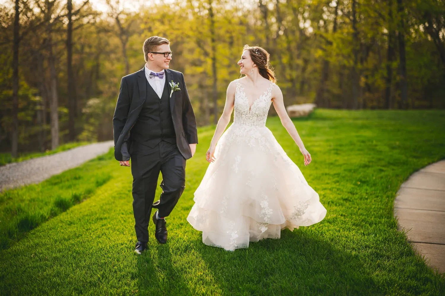 Bride and groom walking together outdoors on their wedding day through green grass surrounded by nature.