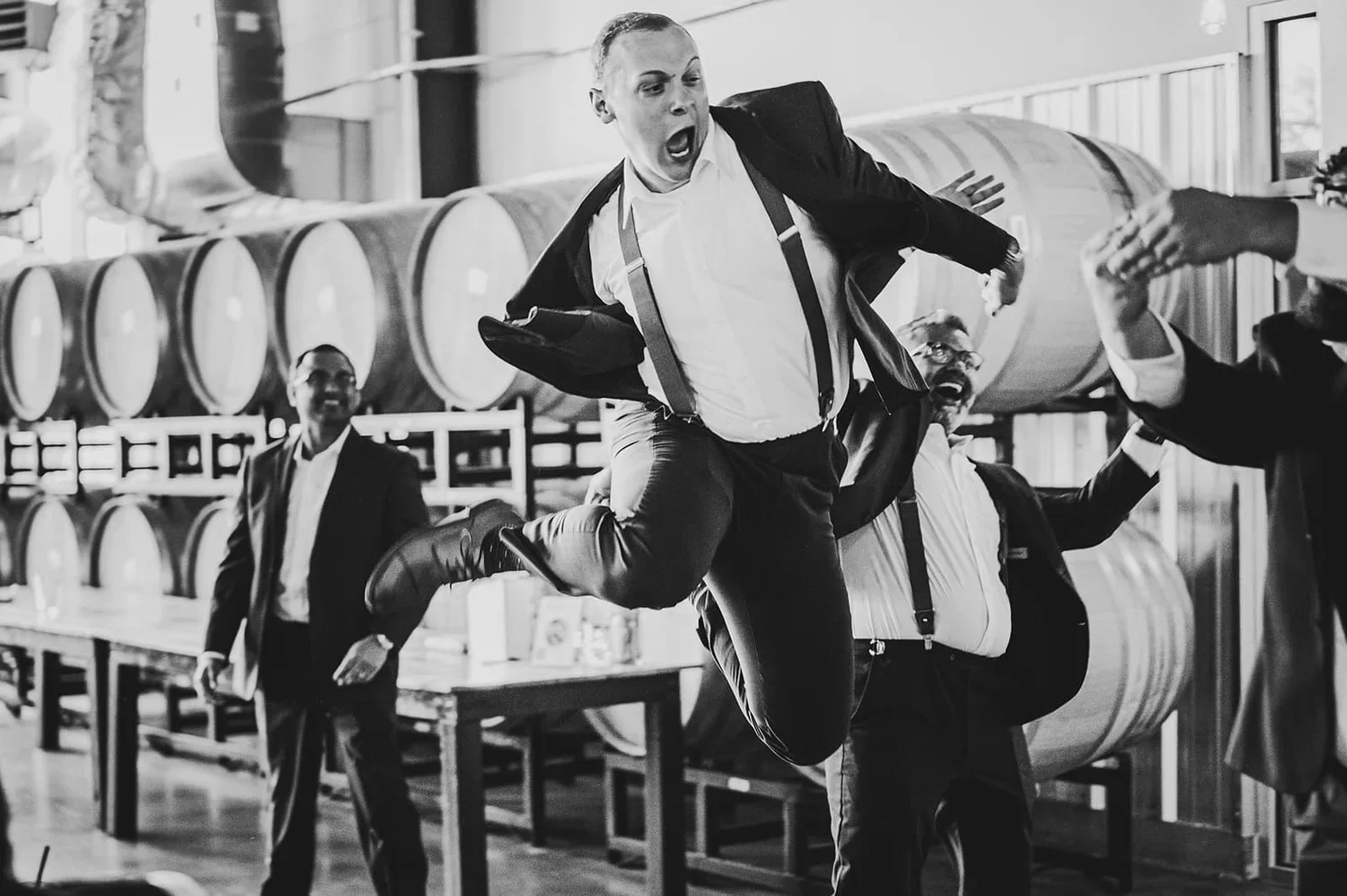Black and white wedding photo of groomsmen having fun and jumping together at the wedding venue.