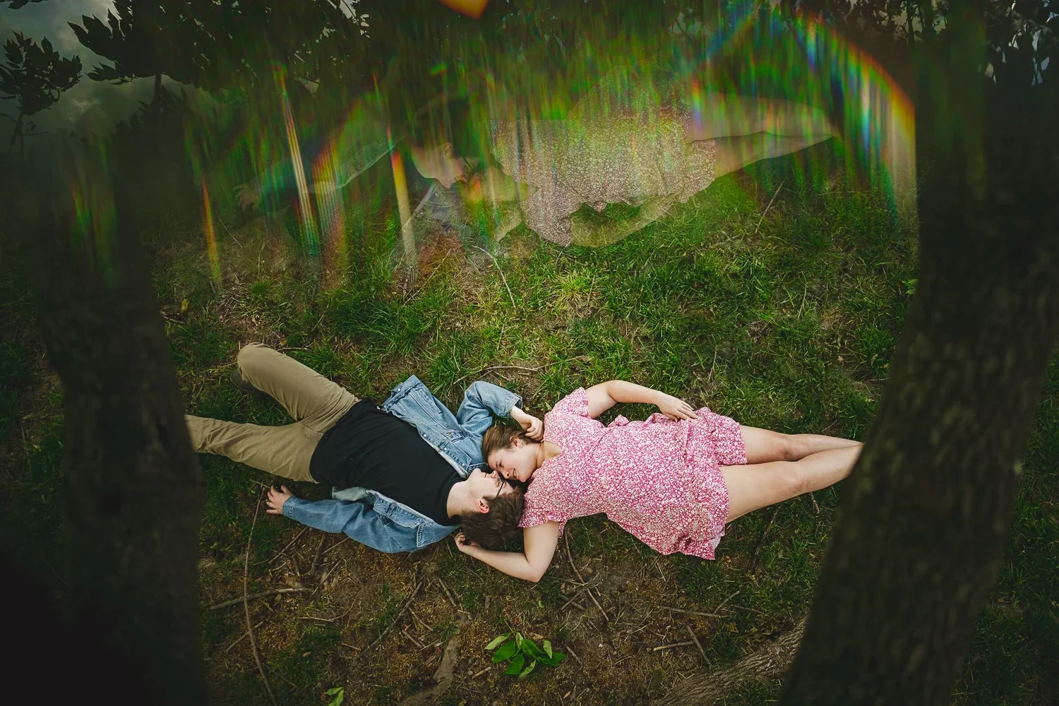 Engagement photo of a couple relaxing side by side on grass, captured from an overhead perspective.