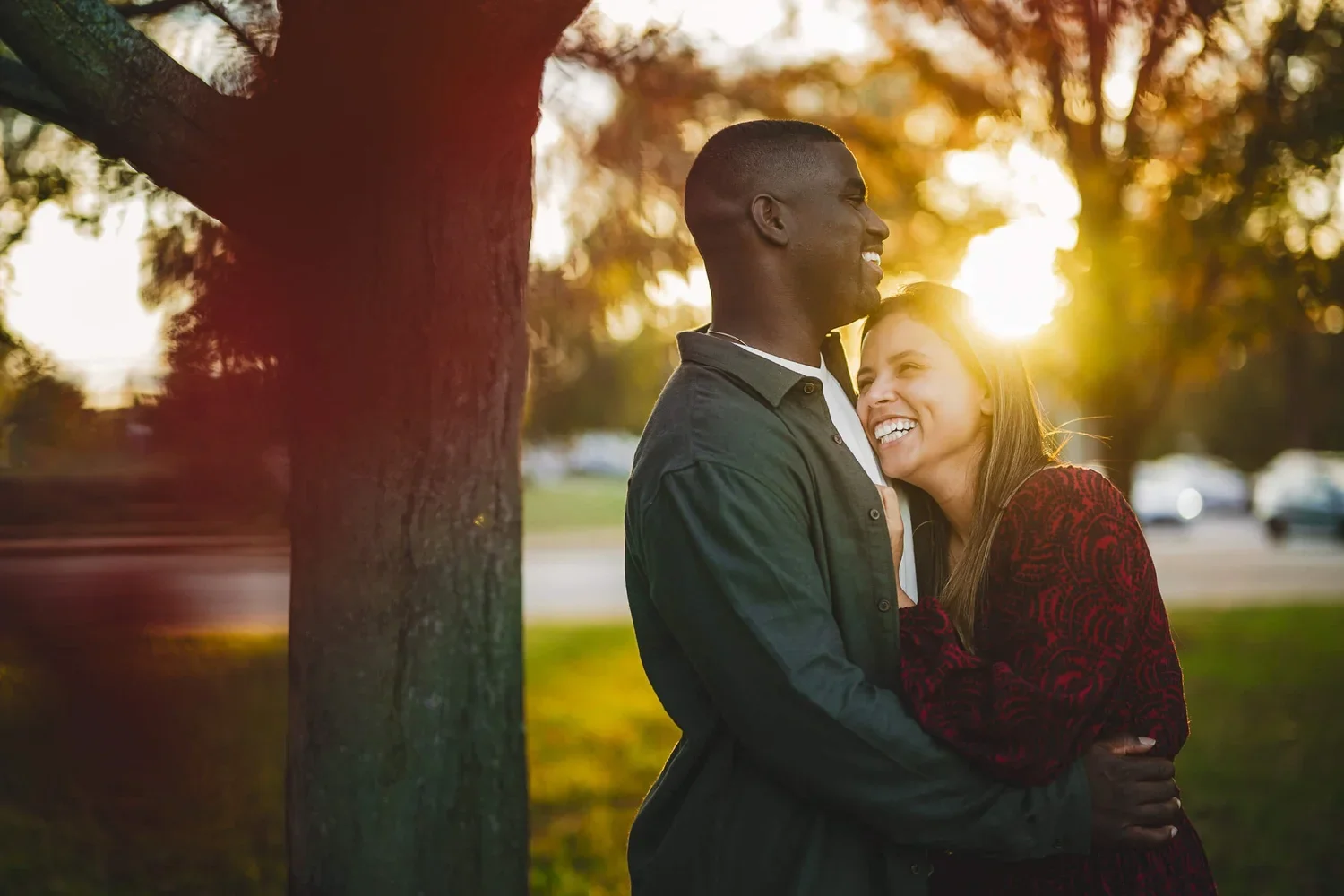 Couple hugging and smiling outdoors during golden hour with the setting sun shining behind them.